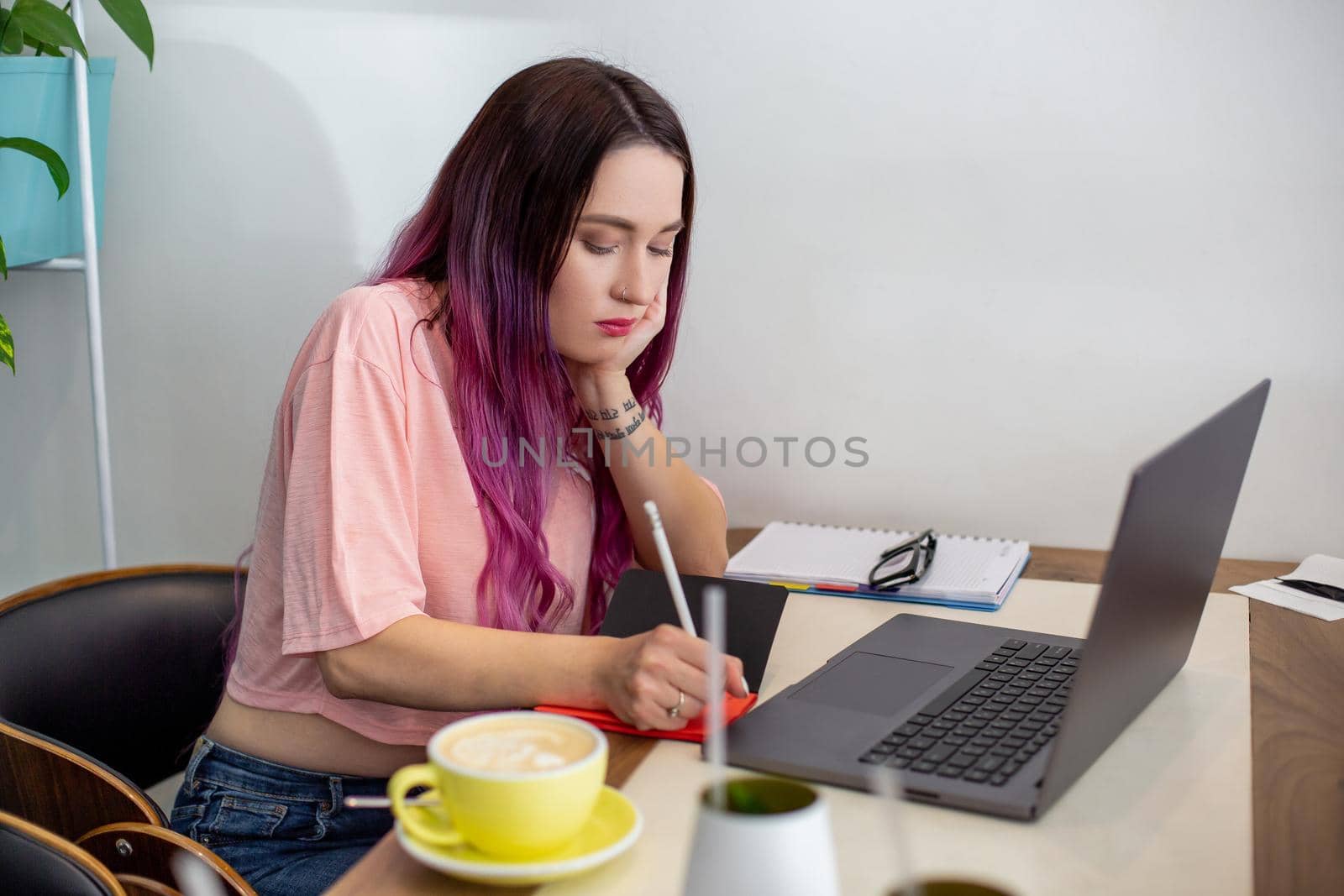 Young woman with pink hair with laptop computer sitting in cafe, intelligent female student working on net-book after her lectures in University