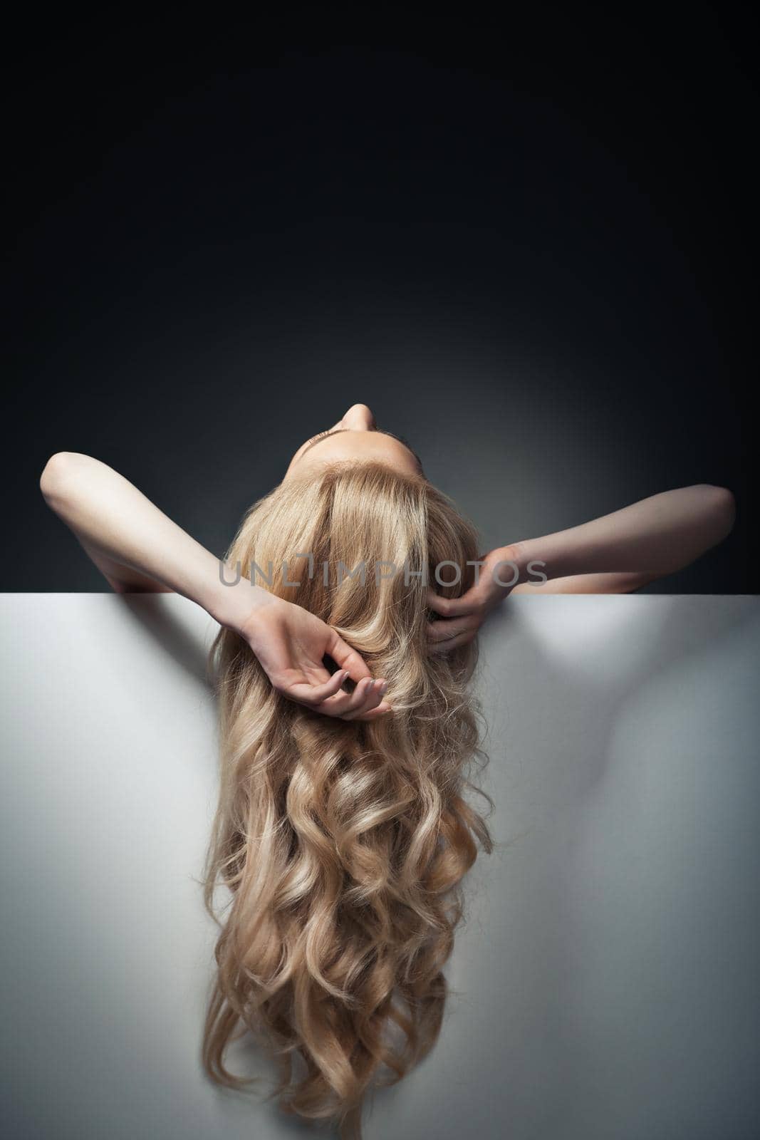 pretty blond model hiding behind a big blank sheet of paper and looking up her hands haging freely.