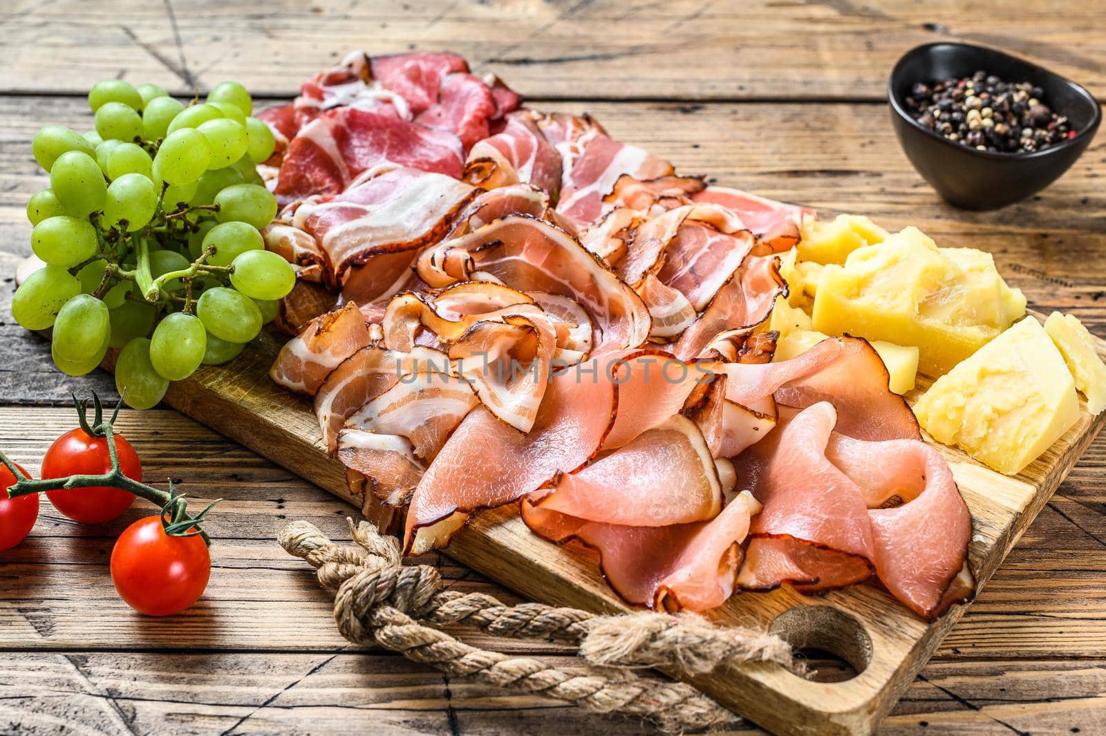 Meat antipasto board, pancetta, salami, sliced ham, sausage, prosciutto, bacon with grape and parmesan cheese. Wooden background. Top view by Composter
