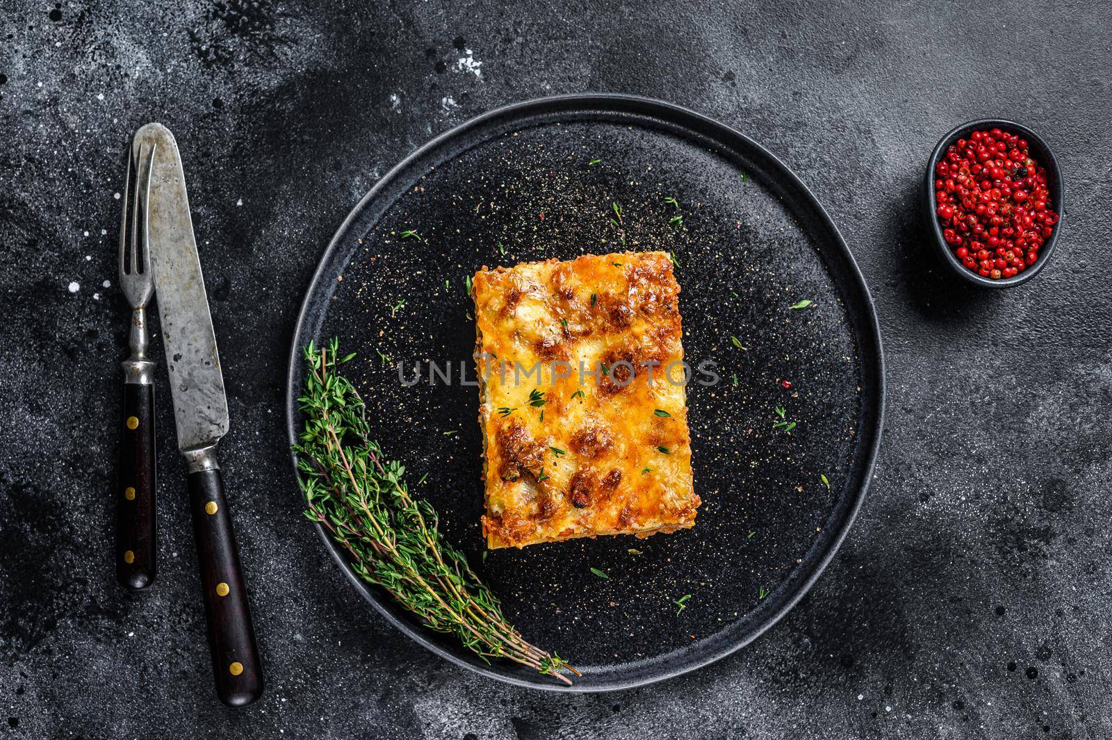 Lasagna with mince beef meat and tomato bolognese sauce on a plate. Black background. Top view.