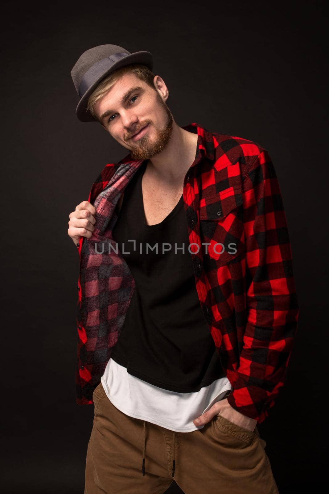 Handsome trendy young guy at the studio on black background. He wears beard and a plaid shirt. Belt portrait