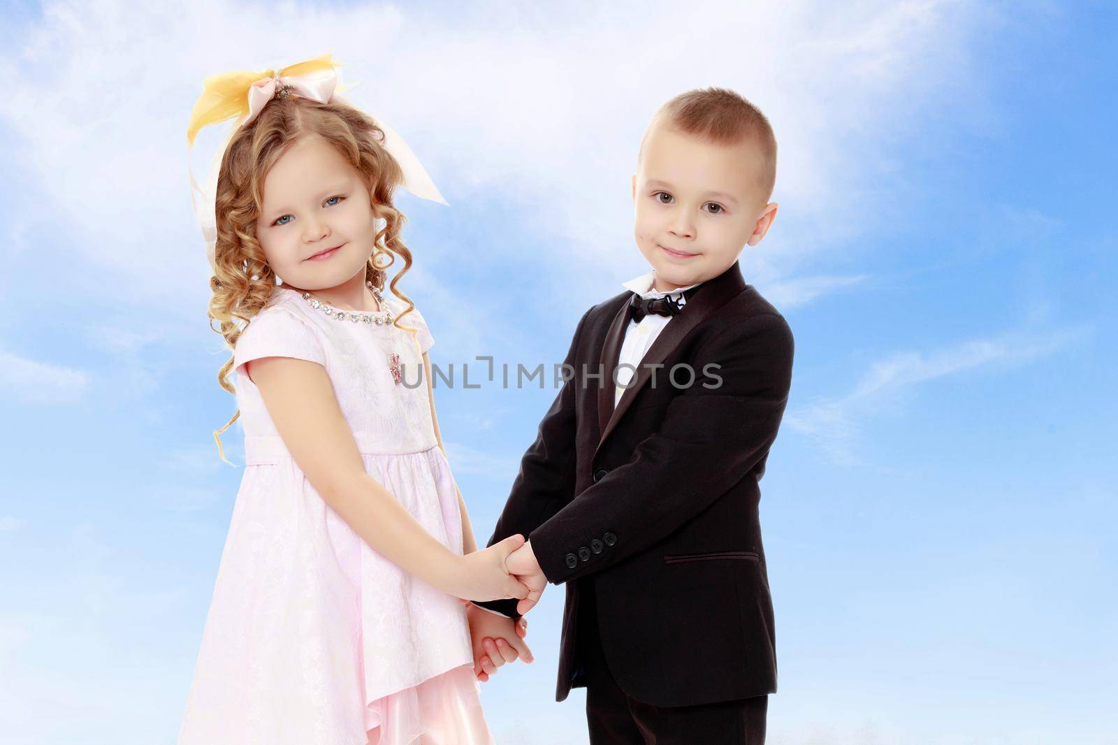 Cute little boy and girl holding hands.On the background of summer blue sky and fluffy clouds.