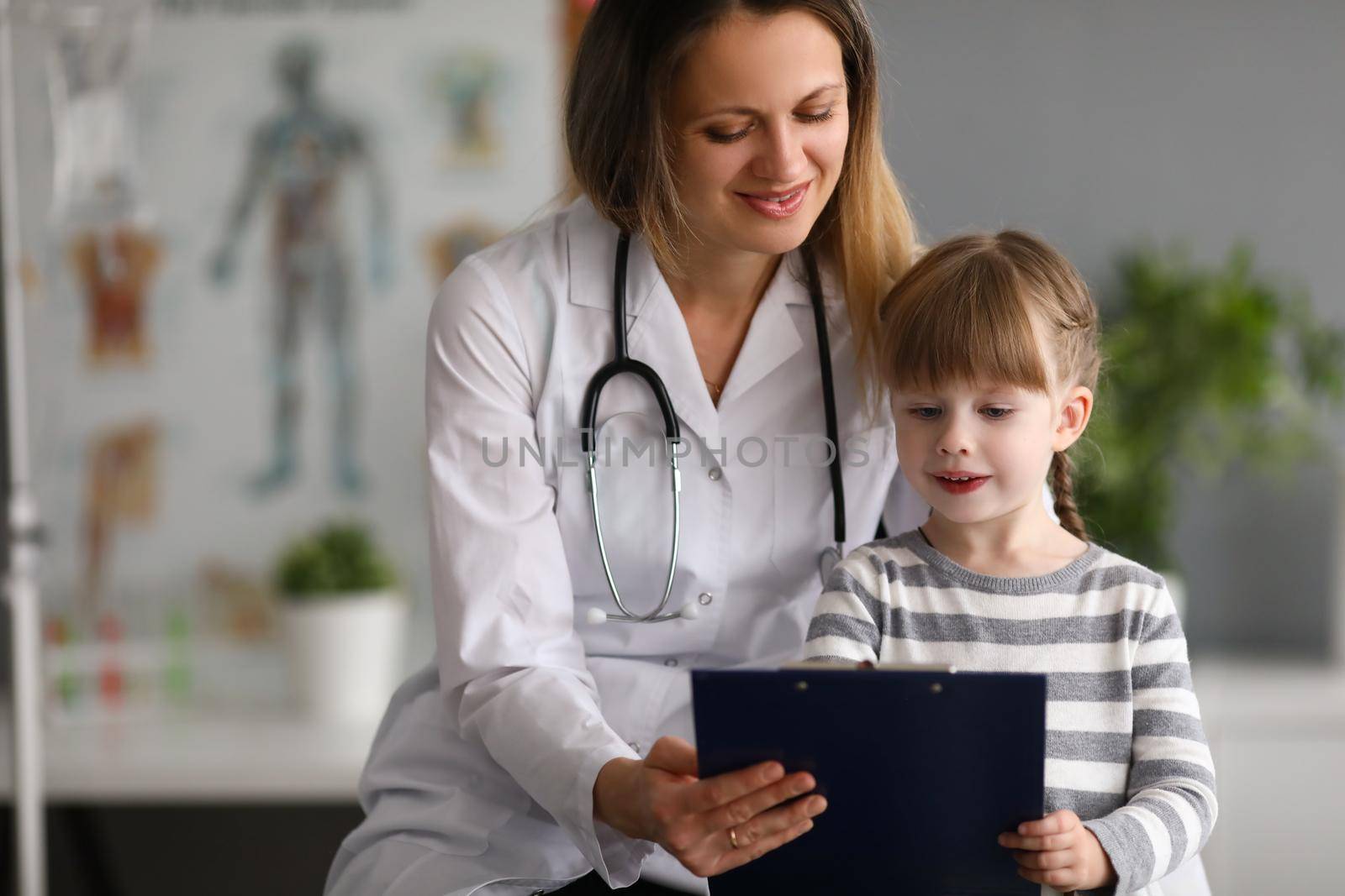 Woman pediatrician doctor communicates with girl shows card in medical office. Medical insurance for children concept