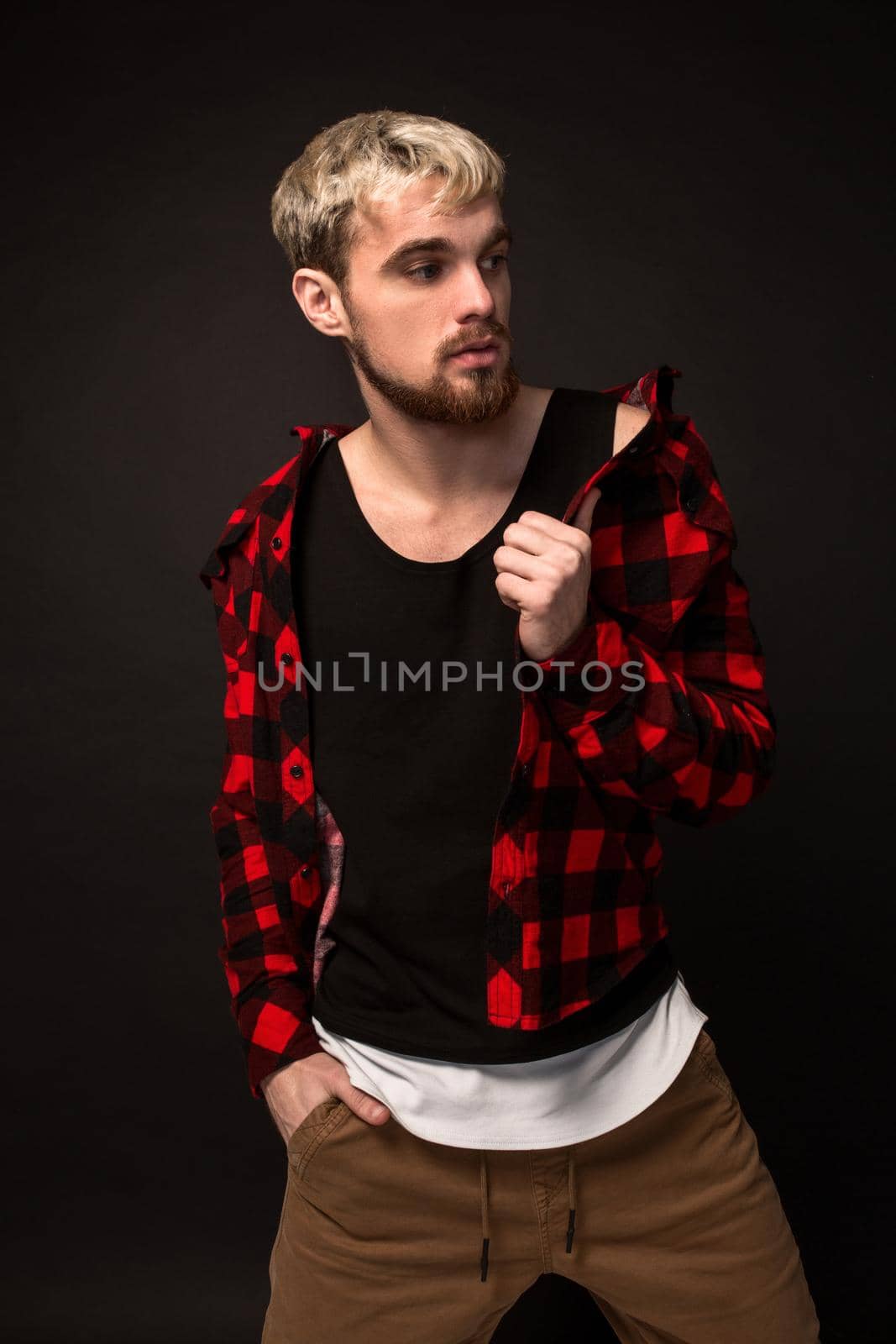 Close-up portrait of attractive young bearded hipster man dressed in shirt in a cage isolated over black background. Studio shot