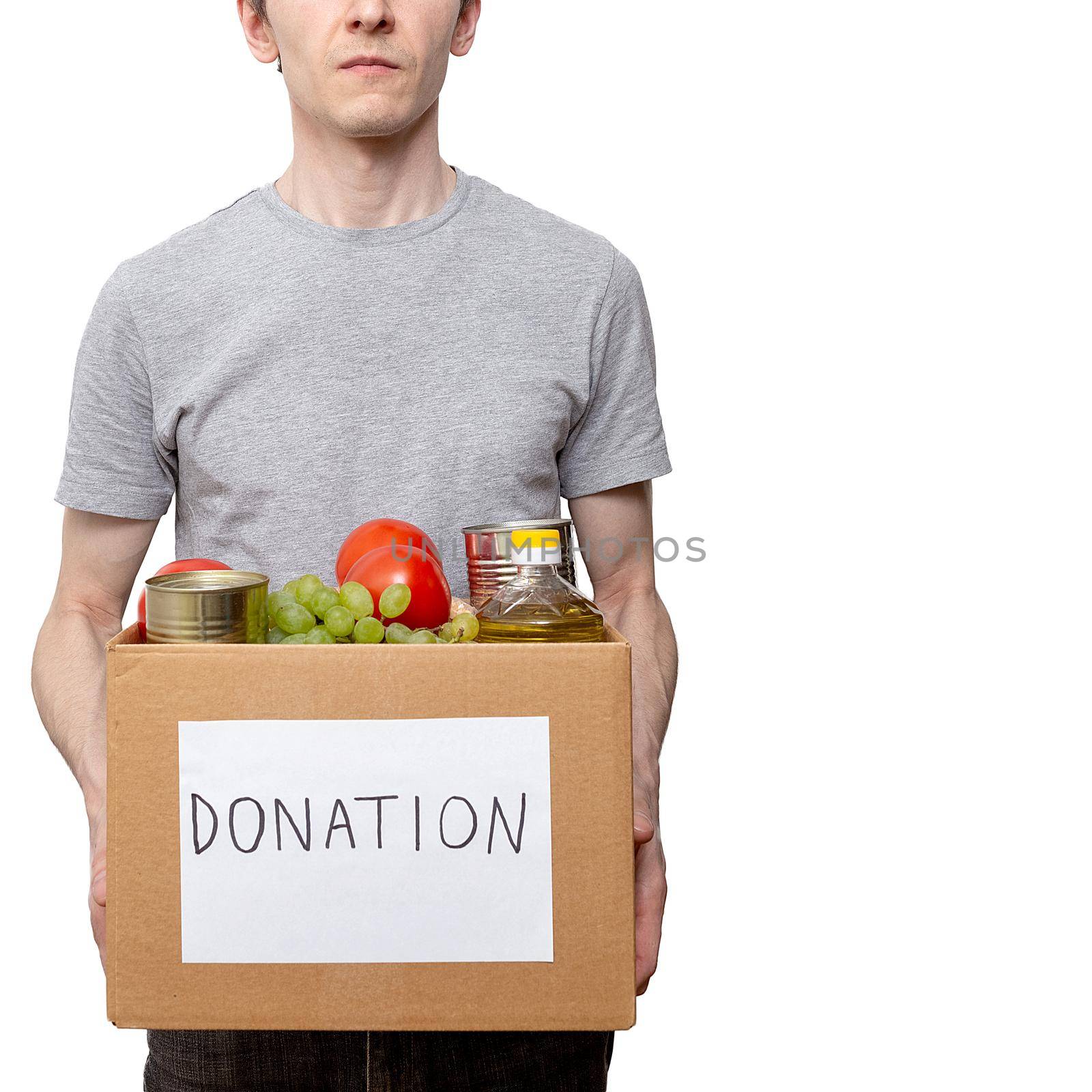Young caucasian man volunteer holding grocery food in carton donation box: vegetable oil, grape, tin cans, tomatoes. Coronavirus relief funds, charity help, delivery, local support. courier worker