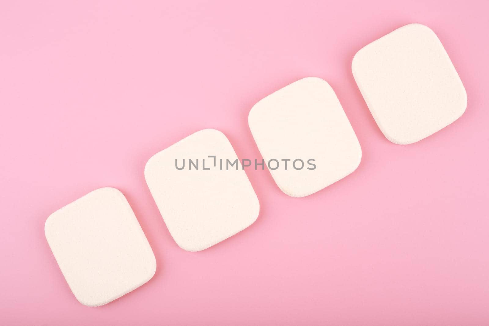 Close up of four make up sponges in diagonal row on bright pink background by Senorina_Irina