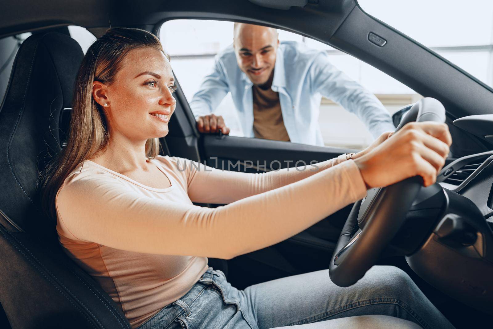 Joyful young couple looking around inside a new car they are going to buy in a car shop dealership