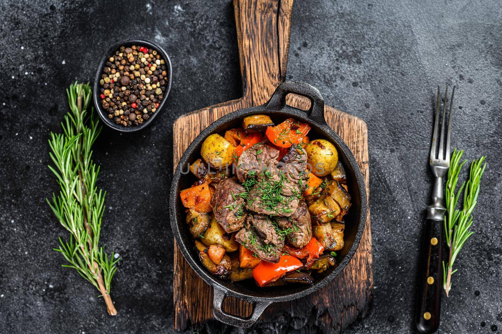 Meat stew in cooking pot on dark rustic cutting board. Black background. Top view.