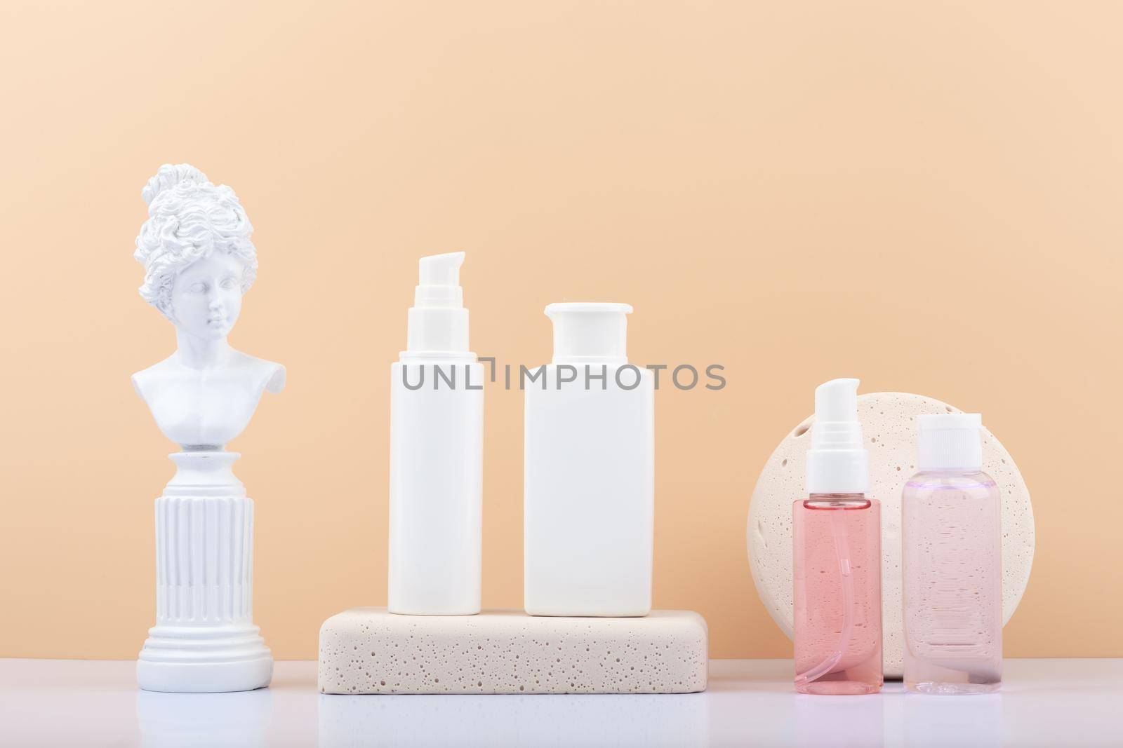 Set of cosmetic products with gypsum figure on white table against beige background. White unbranded cosmetic tubes in a row. Concept of skin care and beauty