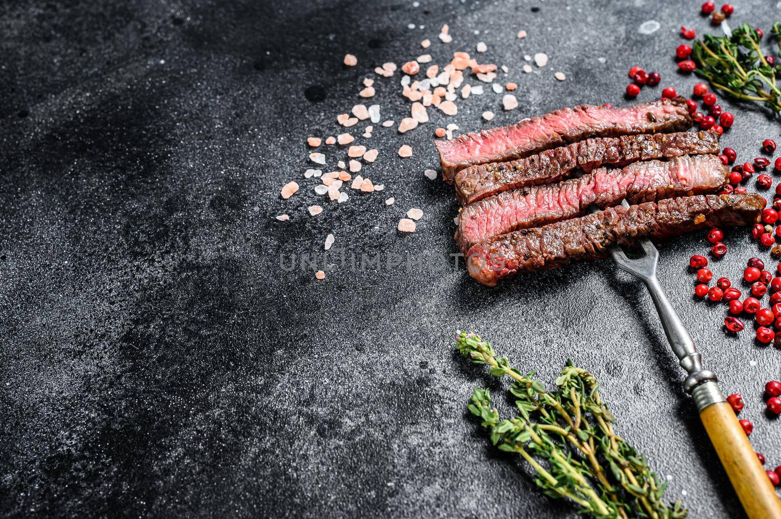 Grilled sliced rib eye steak with spices. BBQ beef. Black background. Top view. Copy space.