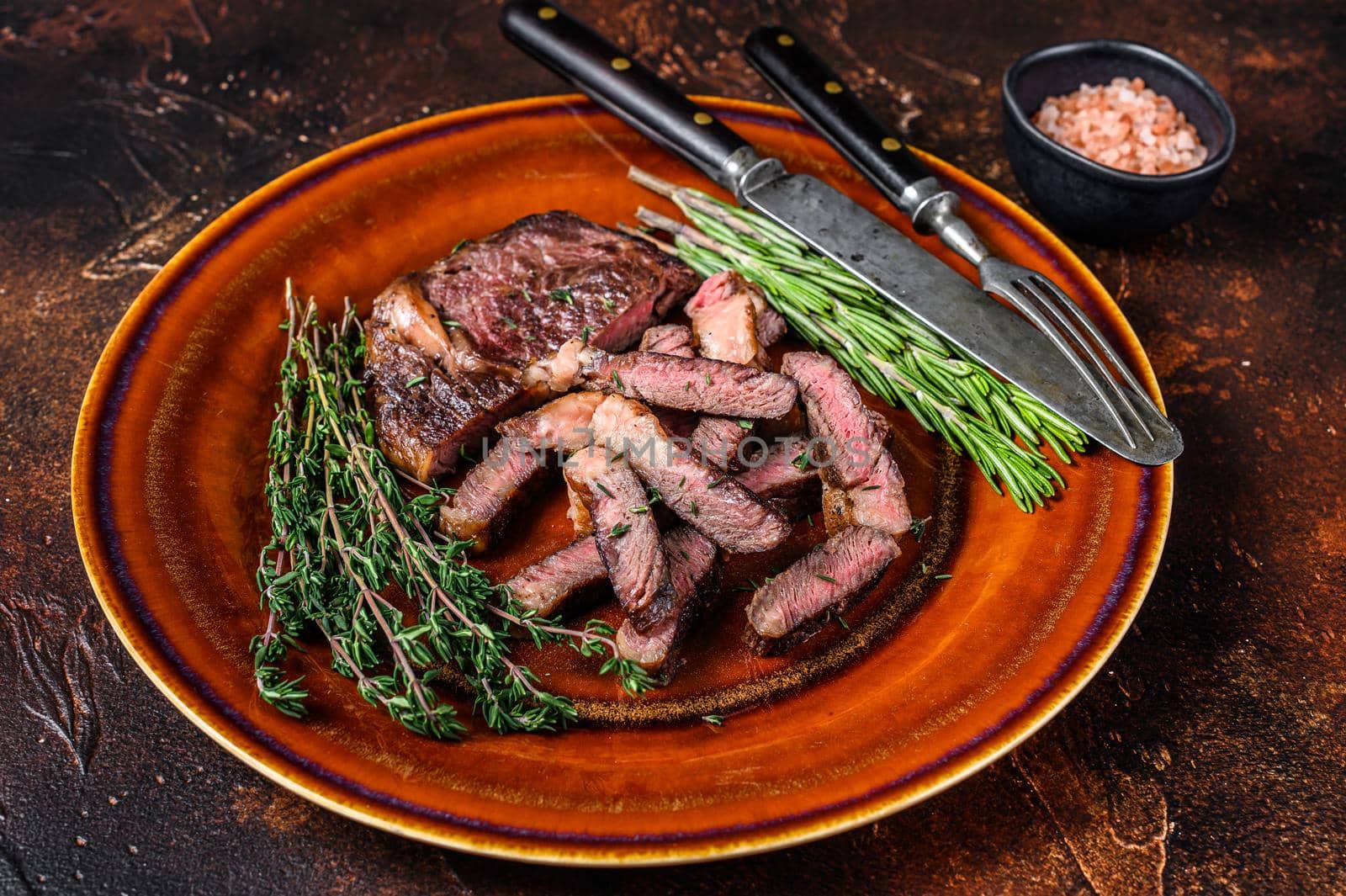 Grilled sliced rib eye or ribeye beef meat steak on a rustic plate. Dark background. Top view.