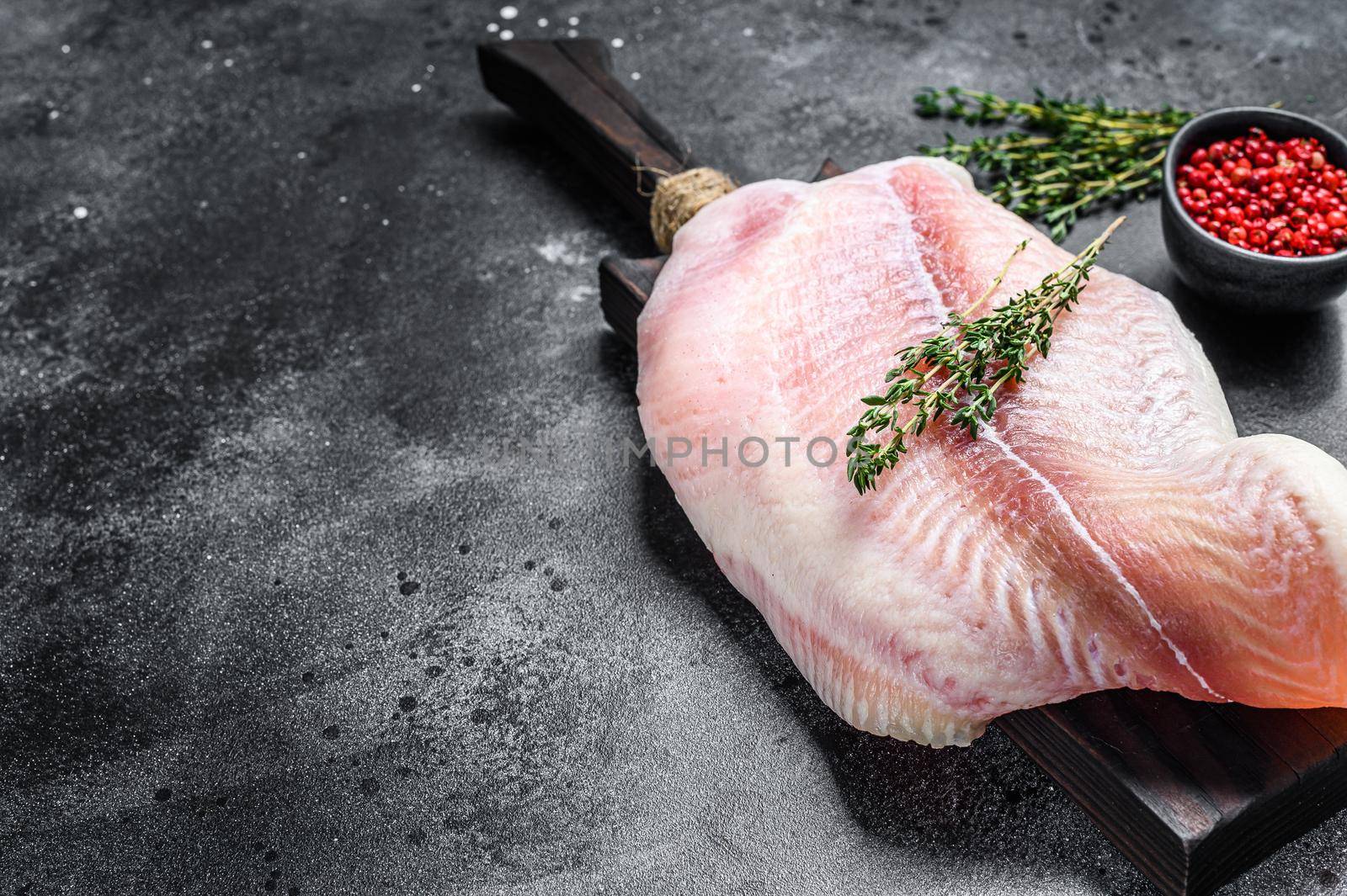 Raw fillet of white fish catfish on a cutting board. Black background. Top view. Copy space.