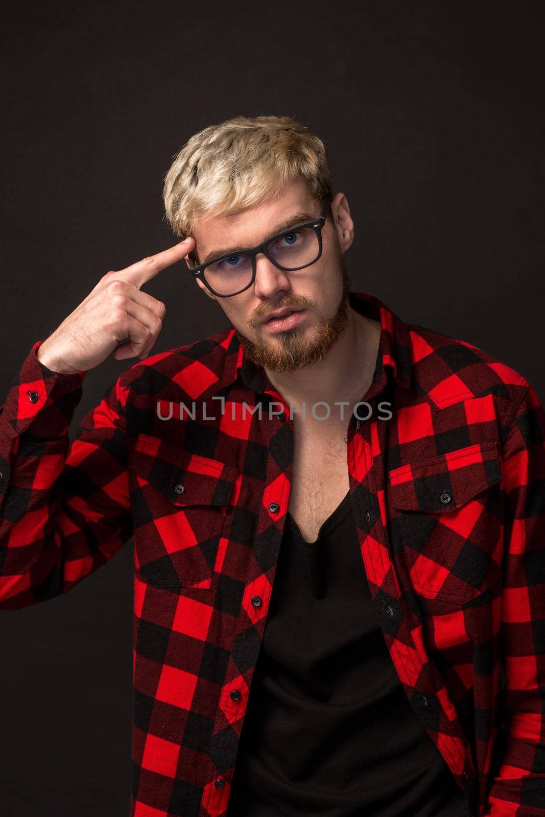 Handsome trendy young guy at the studio on black background. He wears beard and a plaid shirt. A large portrait