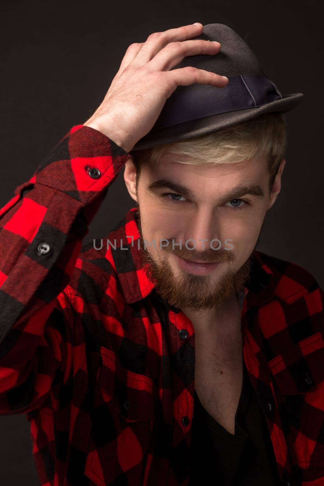 Handsome trendy young guy at the studio on black background. He wears beard and a plaid shirt. A large portrait