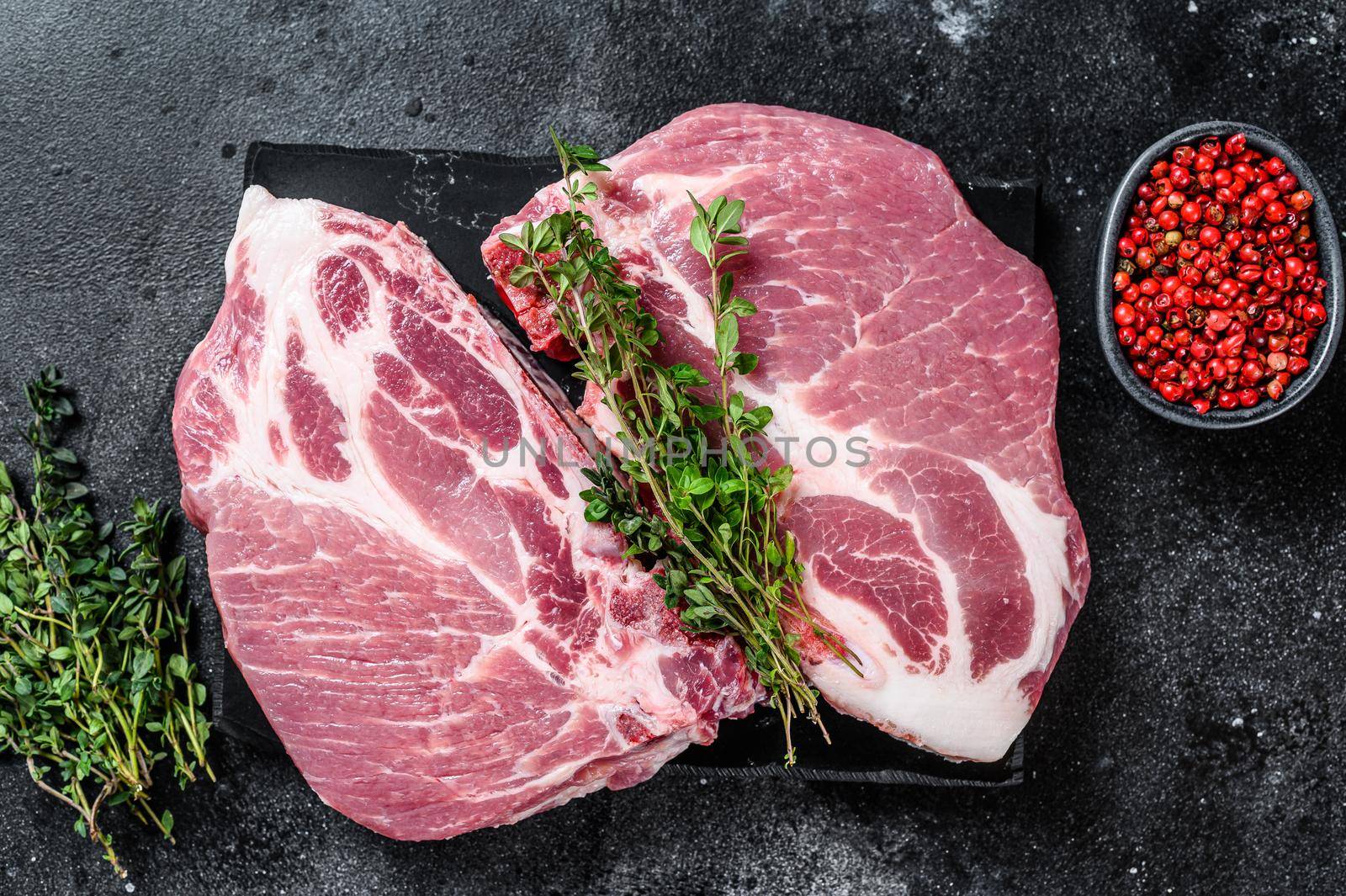Raw pork meat steaks on a marble board. Black background. Top view by Composter
