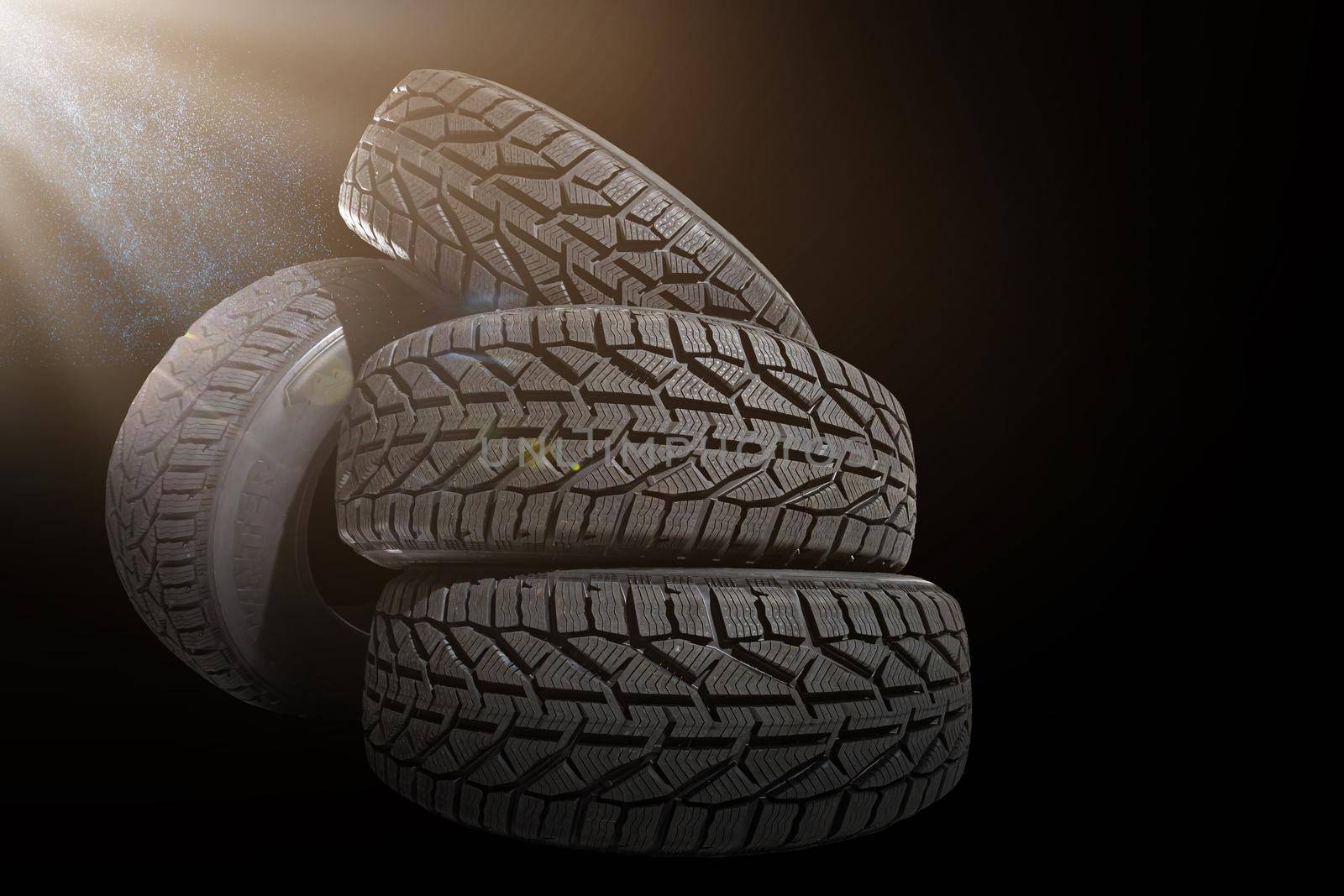 Stack of four new black tyres for winter car on black background by Andelov13