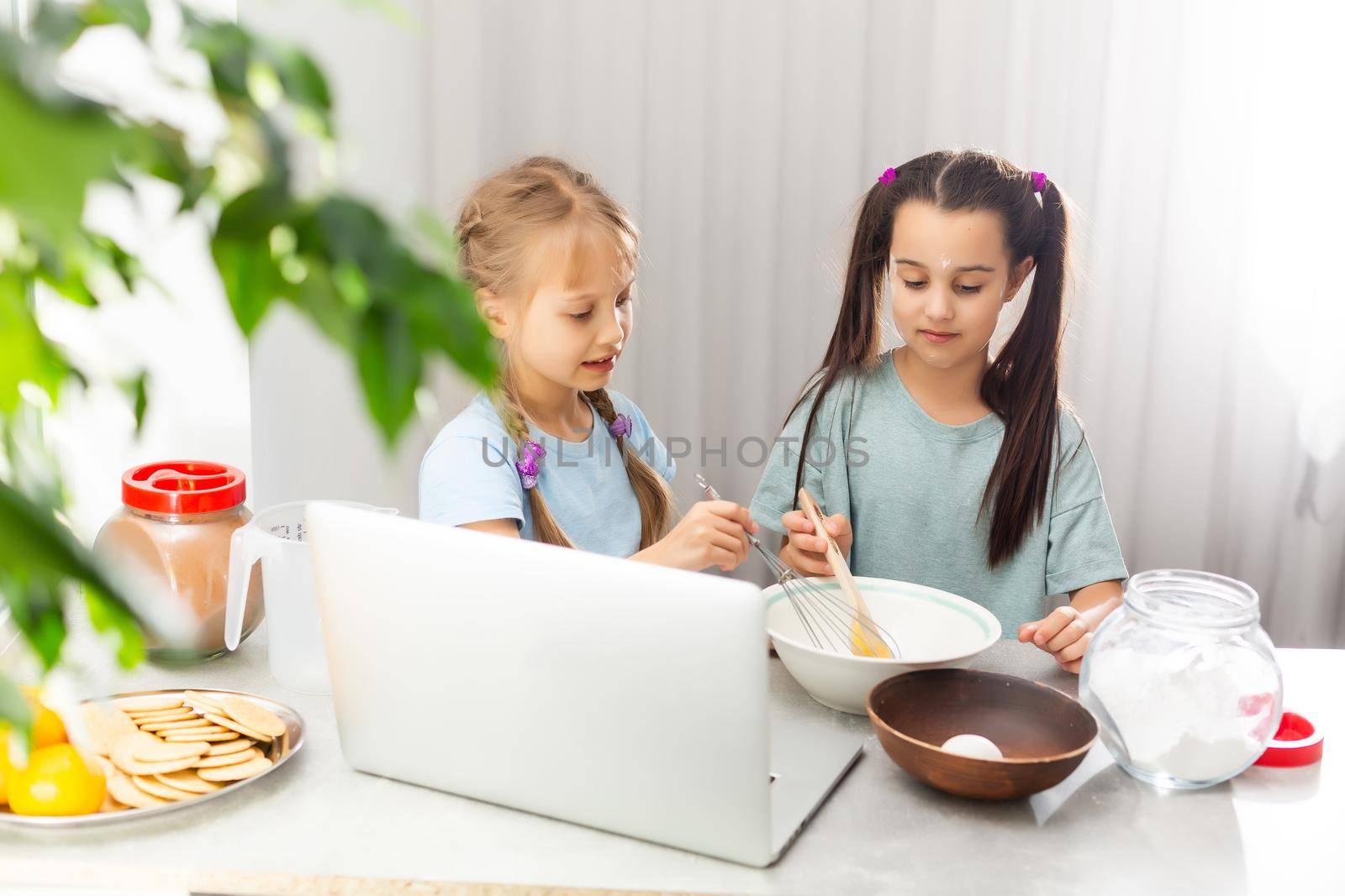 two girls learn to cook on a laptop online, watching video, smiling by Andelov13