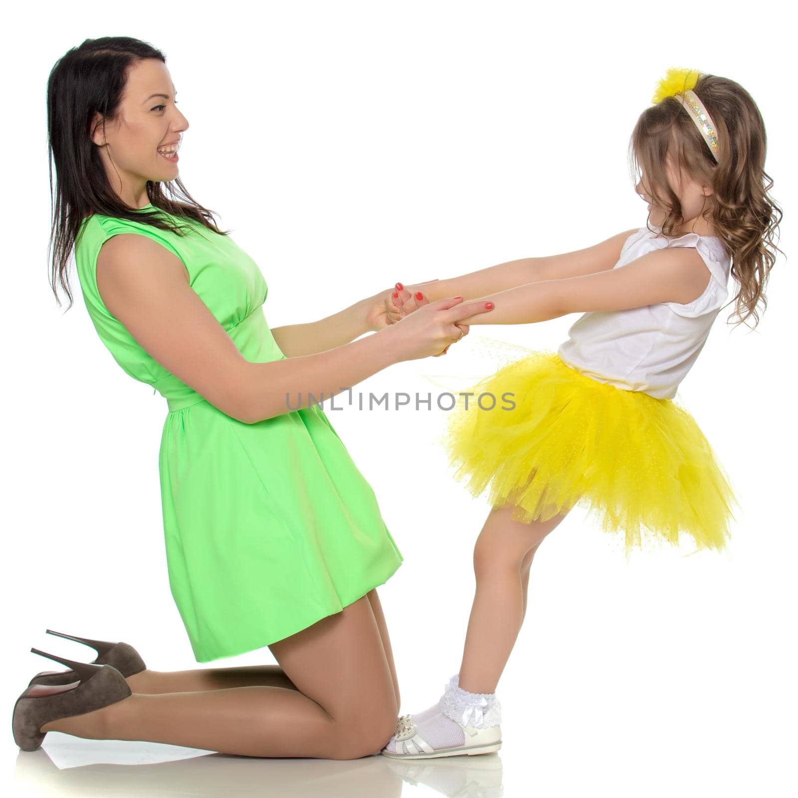 Beautiful young mother in a short green dress and her little beloved daughter in a yellow skirt.They have fun holding hands.Isolated on white background.