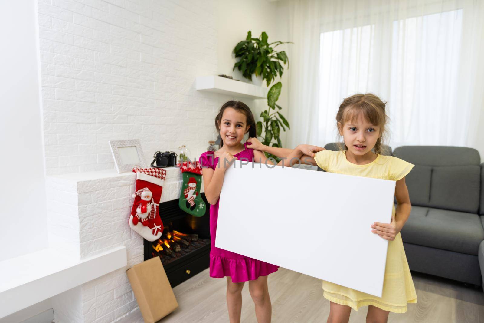 Christmas kids standing with empty horizontal banner in hands, two little girls holding a photo canvas
