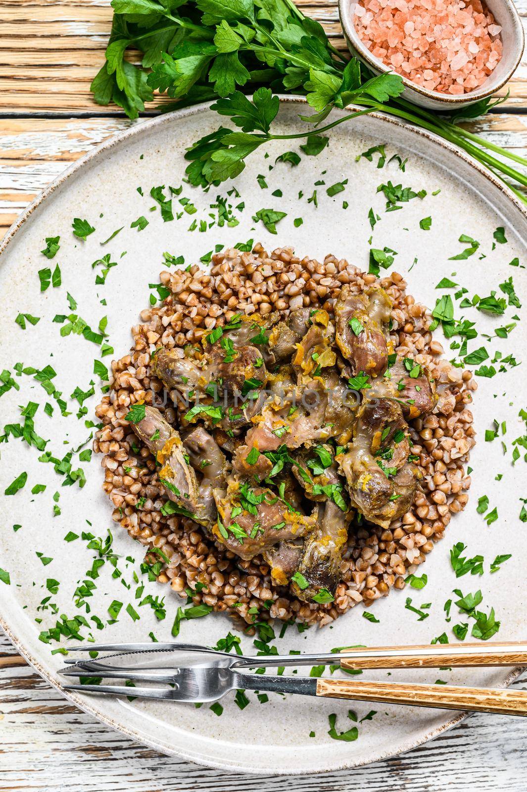 Stewed chicken stomachs with vegetables and buckwheat on a plate. Wooden white background. Top view.