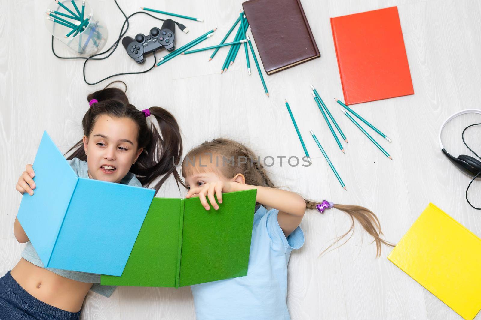 two little girls sisters reading a book lying on the floor