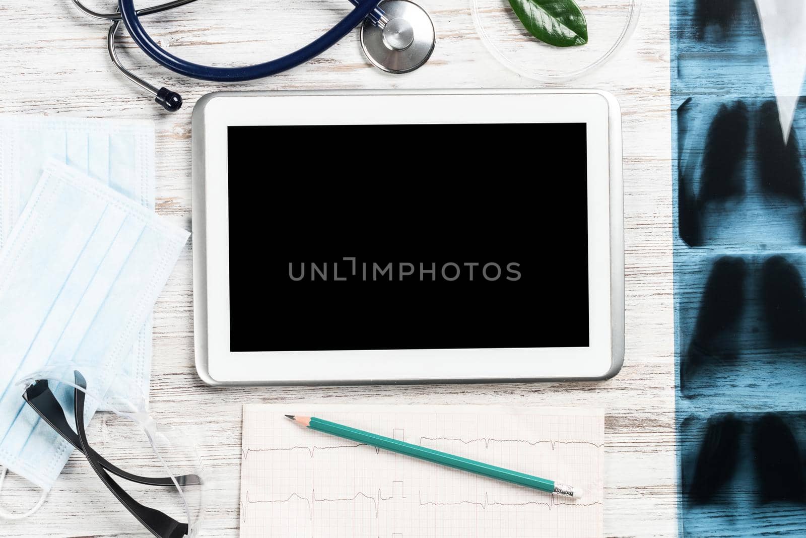 Flat lay workplace of doctor in modern clinic. Tablet computer with blank screen, x-ray image, stethoscope and cardiogram lies on wooden desk. Professional medical consultation and treatment