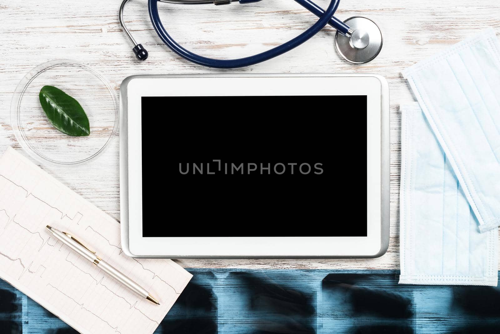 Mock up of doctors desktop with medical supplies. Tablet computer, x-ray image, stethoscope and cardiogram lies on wooden desk. Professional healthcare technology. Medical consultation and treatment.