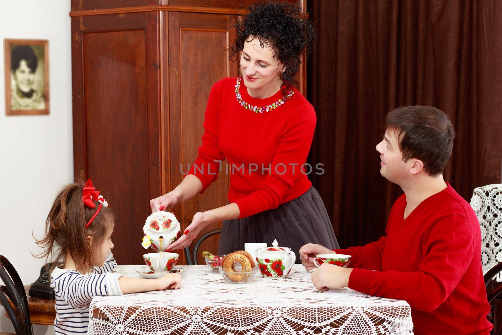 A family of three in the interior of the fifties of the last century, drinking tea for lace tablecloth vintage oak table.