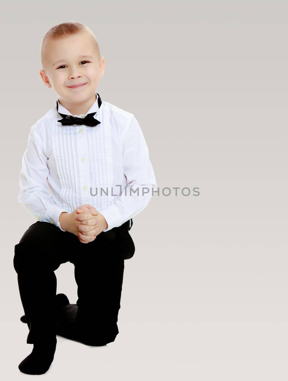 Beautiful , elegant little boy in black pants , white shirt and black tie.On a gray background.