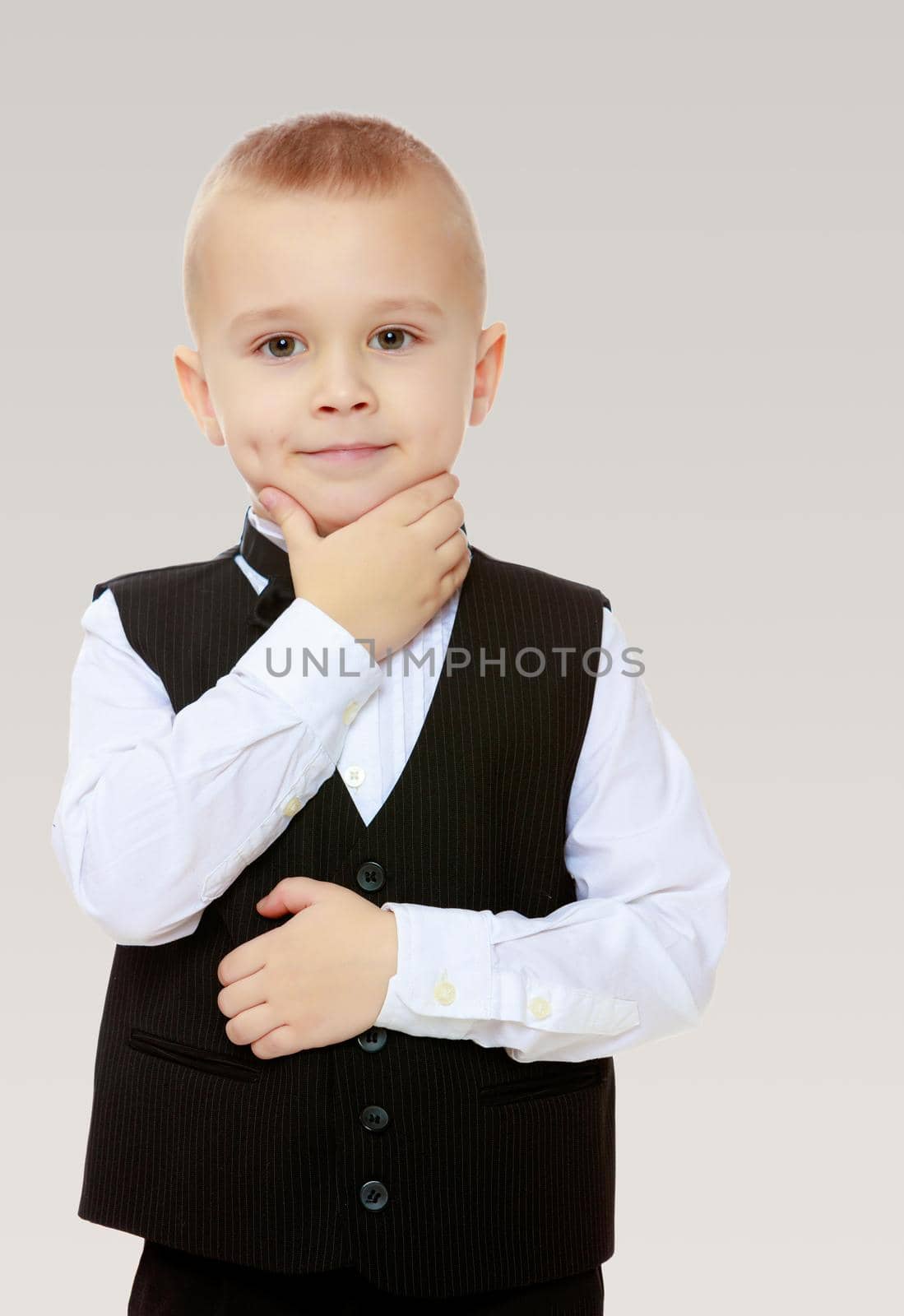 Beautiful little blond boy in a fashionable black suit with a tie.Boy what a thought.On a gray background.