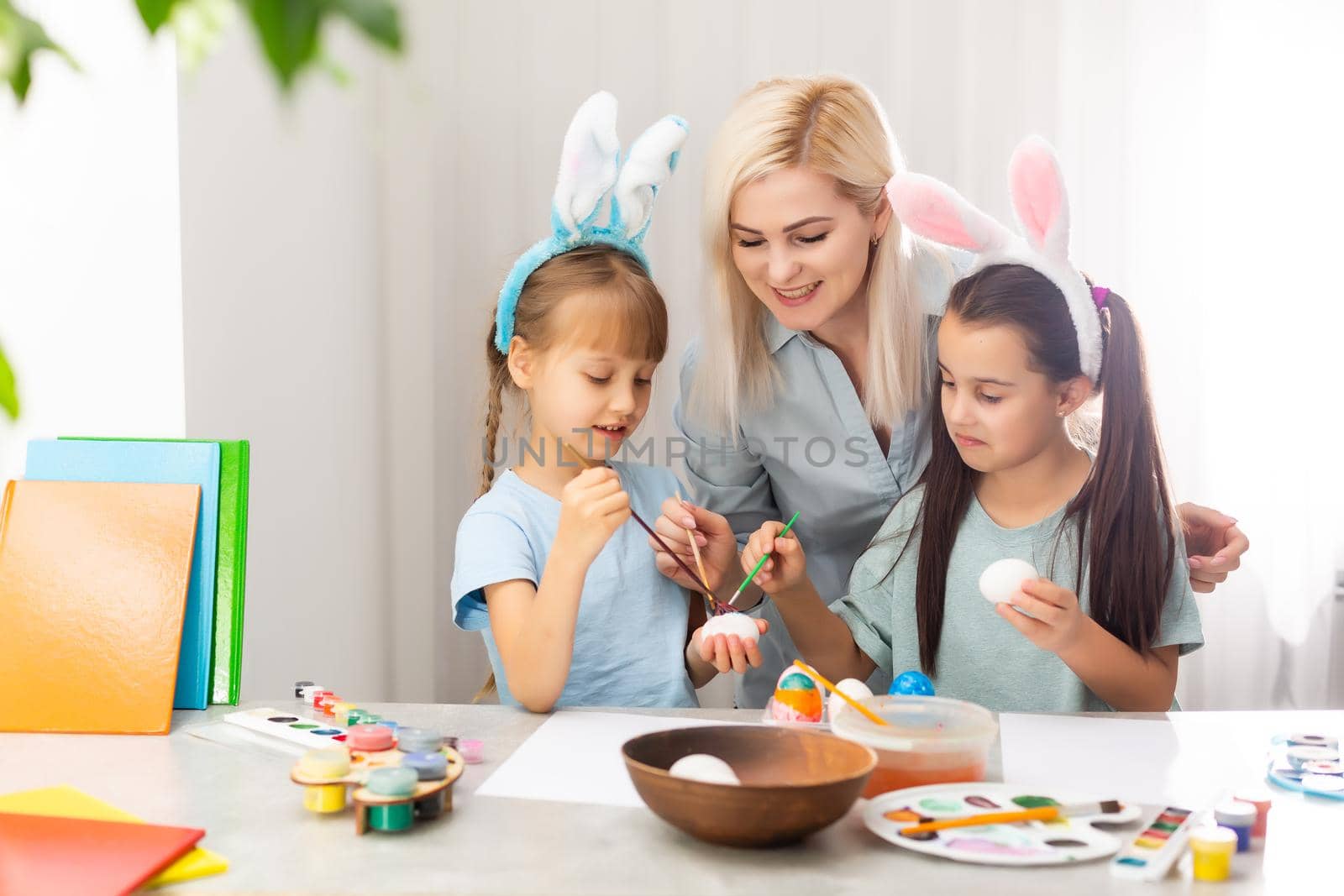 Young mother and her two daughters painting Easter eggs