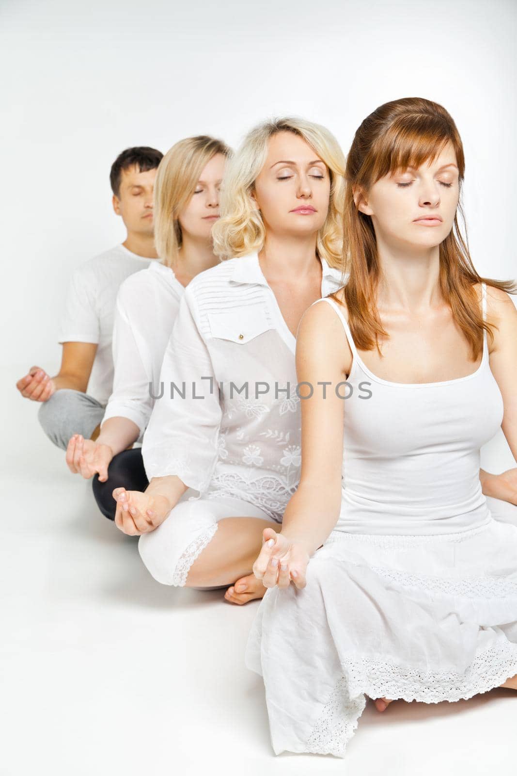 Group of people relaxing and doing yoga in white studio