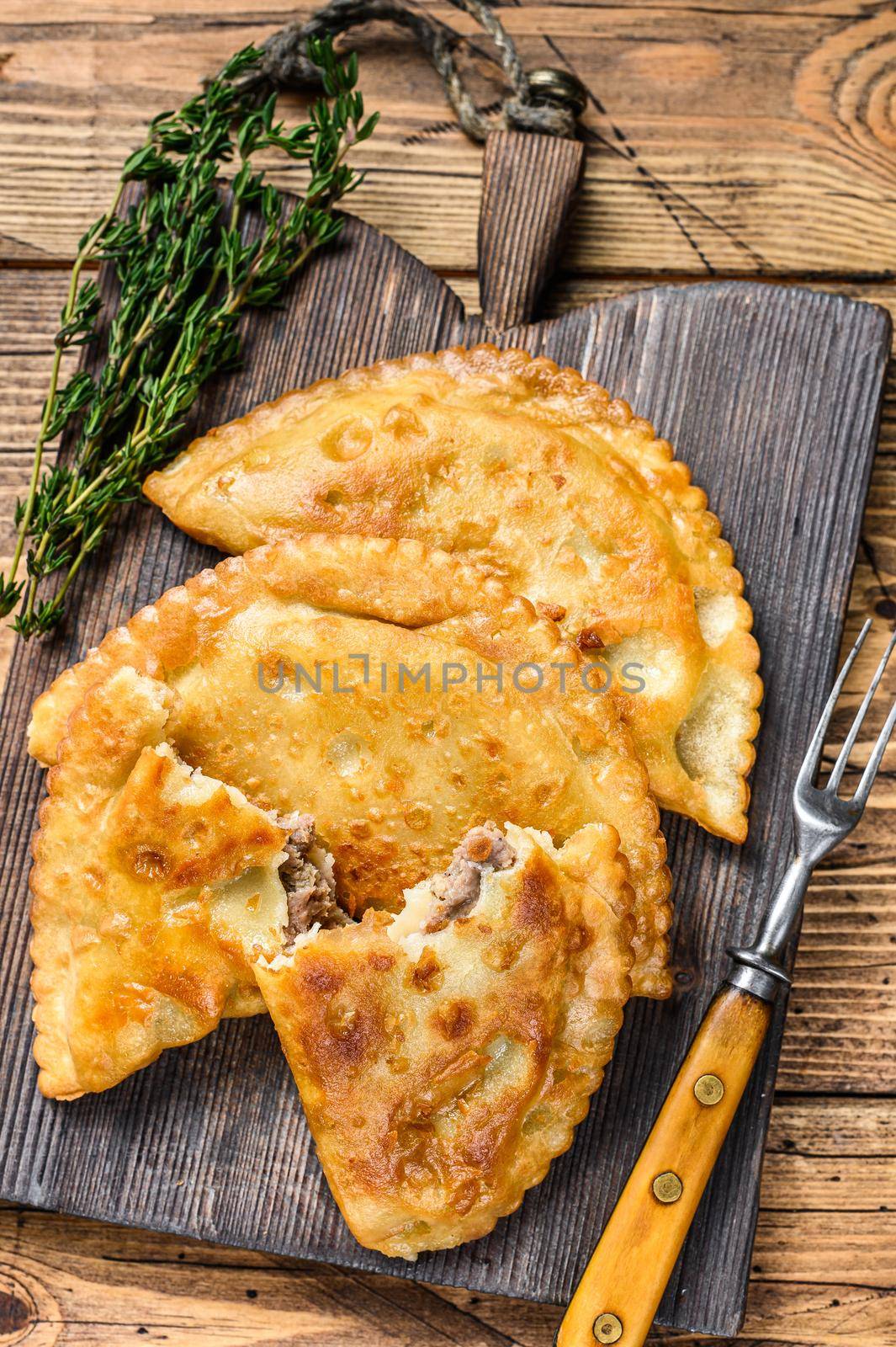 Chilean fried empanadas filled with minced beef meat served on a wooden cutting board. Wooden background. Top view by Composter