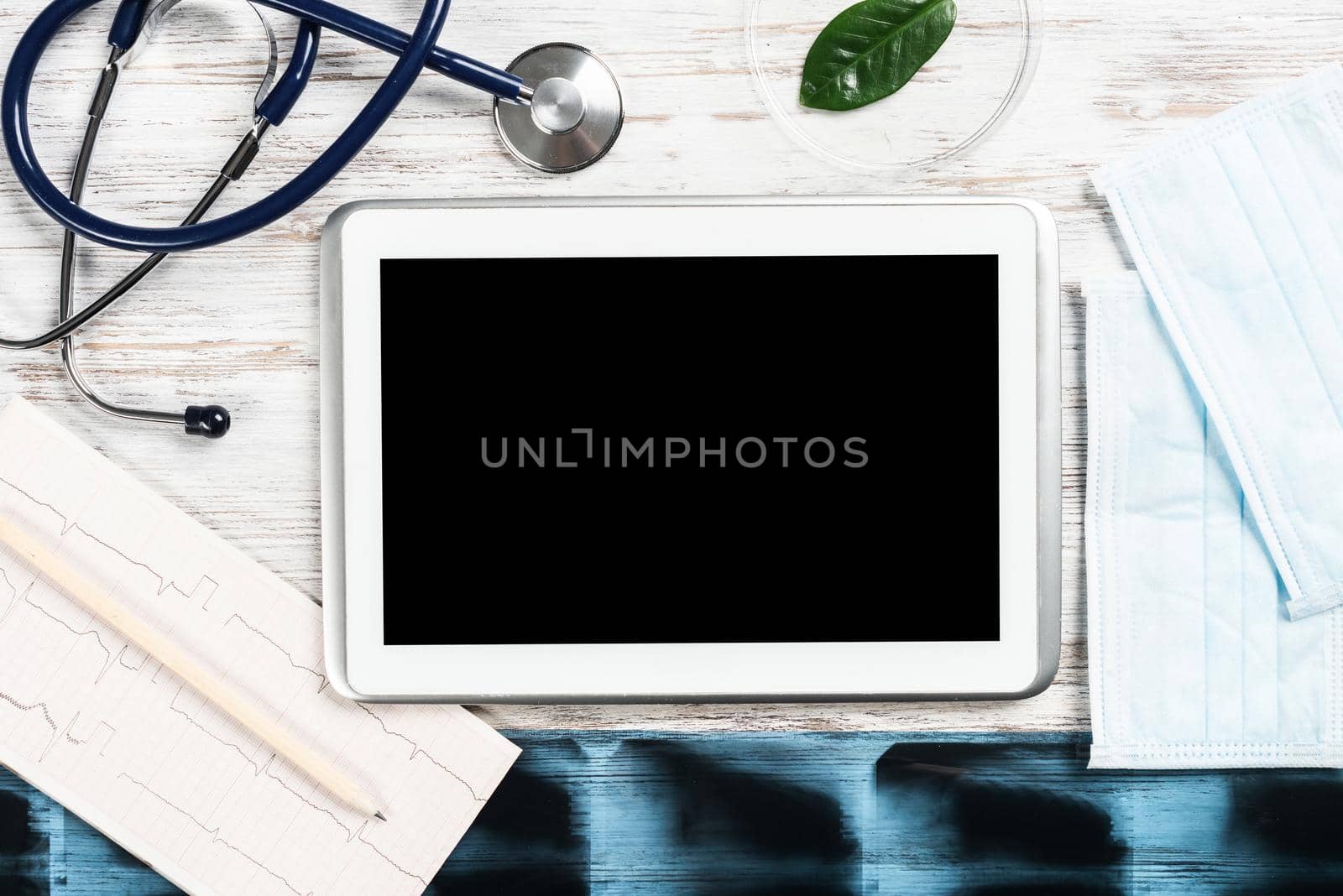 Medical diagnostics in modern hospital. Top view tablet computer with blank screen, x-ray images, stethoscope and cardiogram on wooden desk. Professional healthcare and digital technology in clinic.