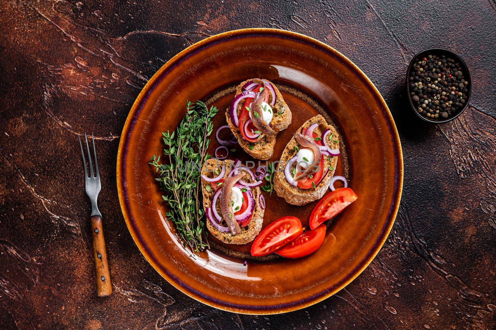 Spanish tapas on bread with olive oil, herbs, tomatoes and spicy anchovy fillets. Dark background. Top view.