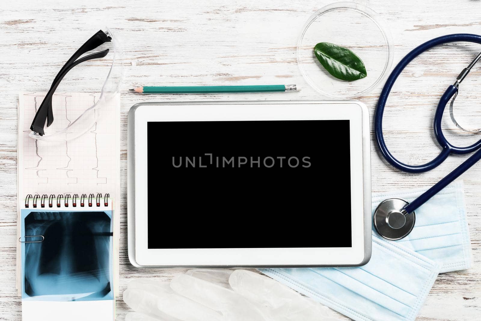 Flat lay workplace of doctor in modern clinic. Tablet computer with blank screen, x-ray image, stethoscope and cardiogram lies on wooden desk. Professional medical consultation and treatment