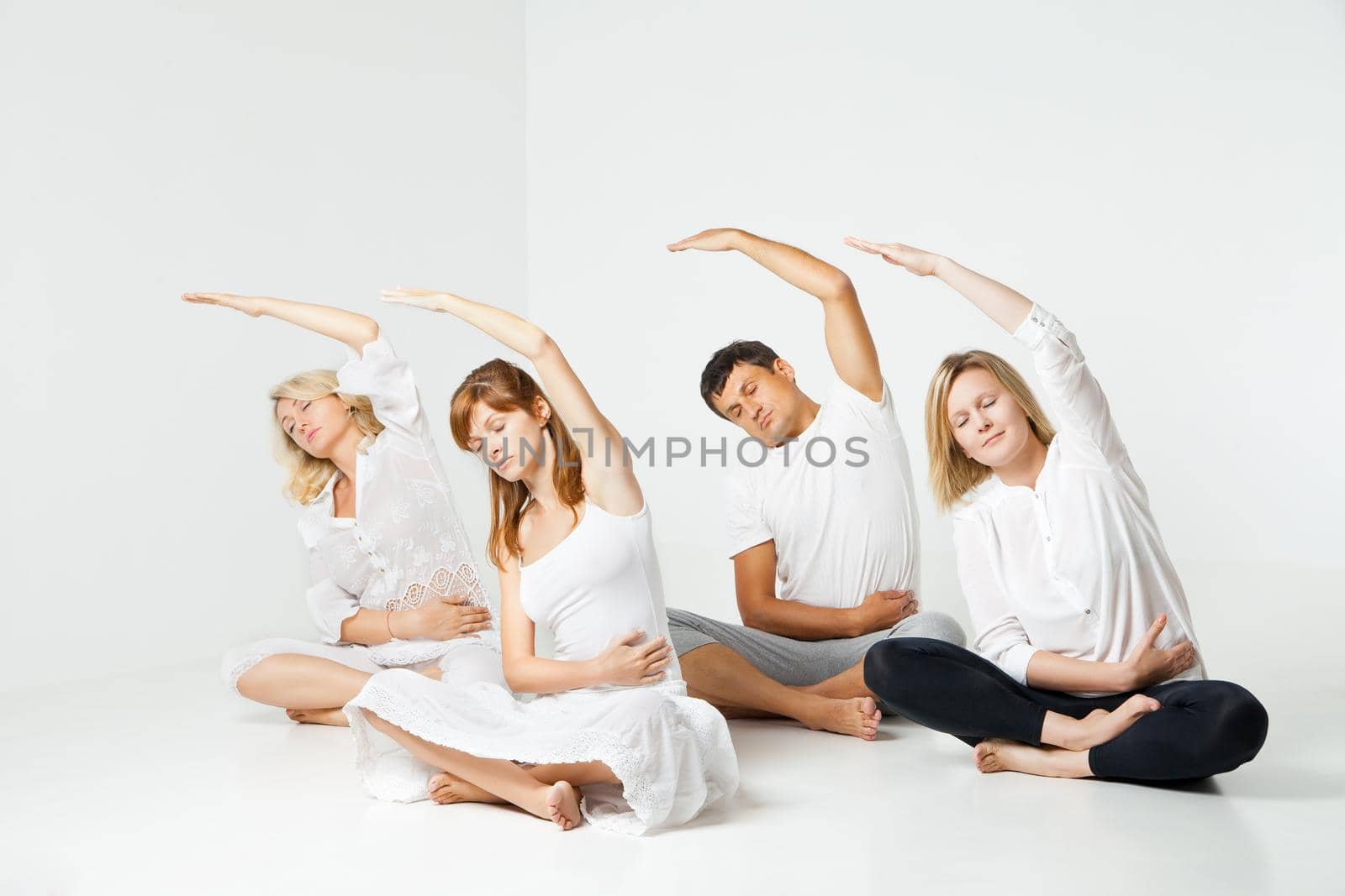 Group of people relaxing and doing yoga in white studio