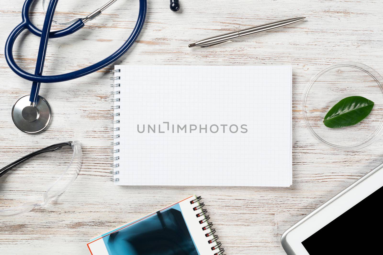 Patient examination and consultation concept with doctor workplace. Tablet computer, x-ray image, notepad, stethoscope and cardiogram on wooden surface. Professional healthcare in medical center.