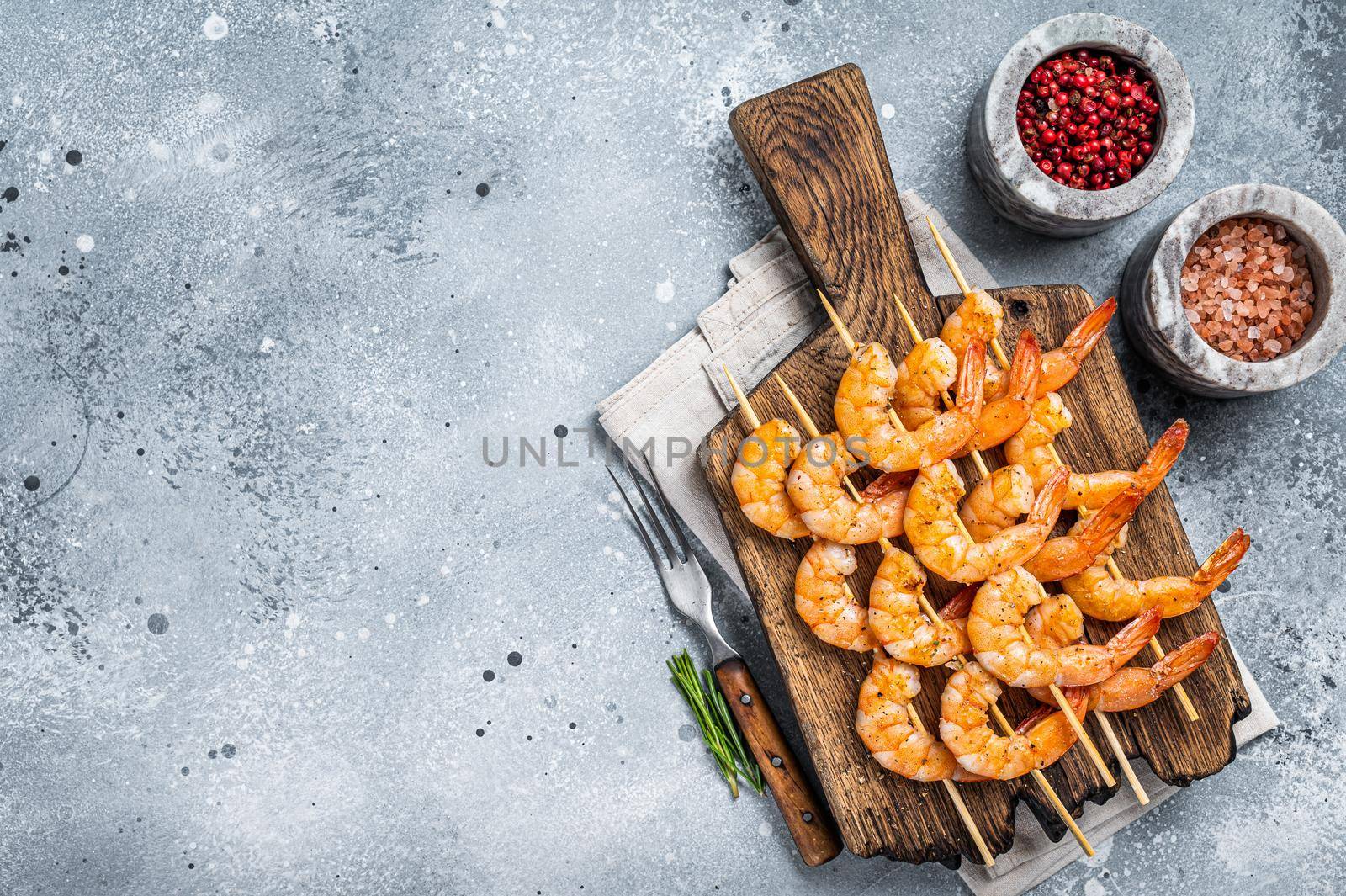 BBQ Roasted shrimps prawns on skewers on a wooden board with herbs. Gray background. Top view. Copy space.
