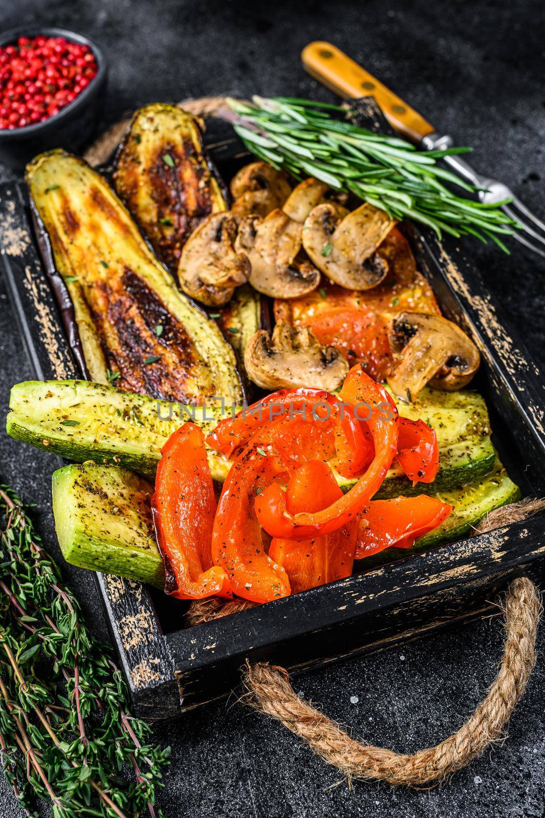 Baked vegetables bell pepper, zucchini, eggplant and tomato in a wooden tray. Black wooden background. Top view.