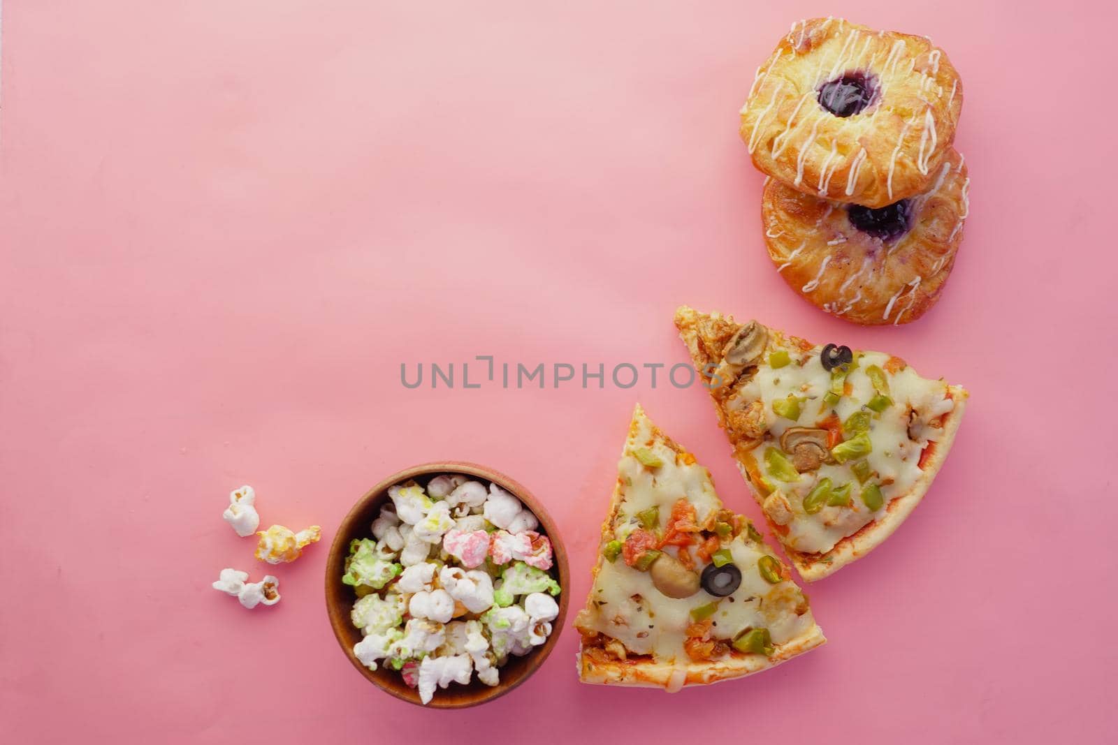 Slice of cheese pizza on a plate , donuts and popcorn on pink ,