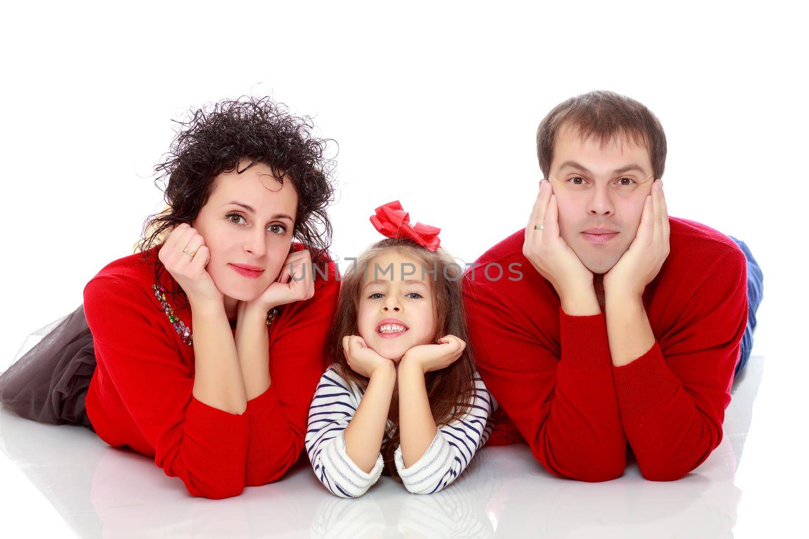 Happy young family dad mom and a little girl in bright red outfits . Family lying on the floor leaning on his hands.Isolated on white background.