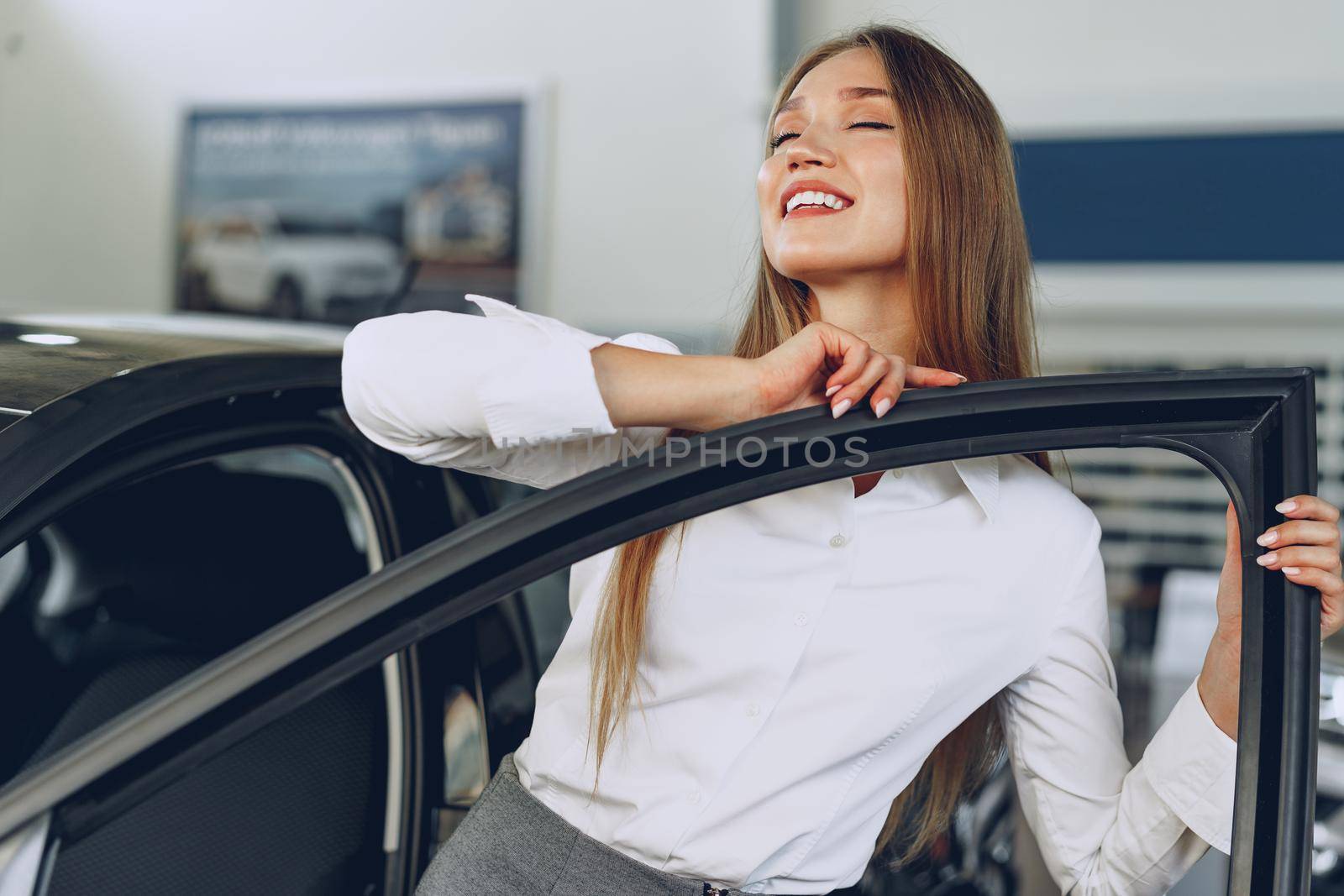 Beautiful young woman touching her new car with pleasure and joy