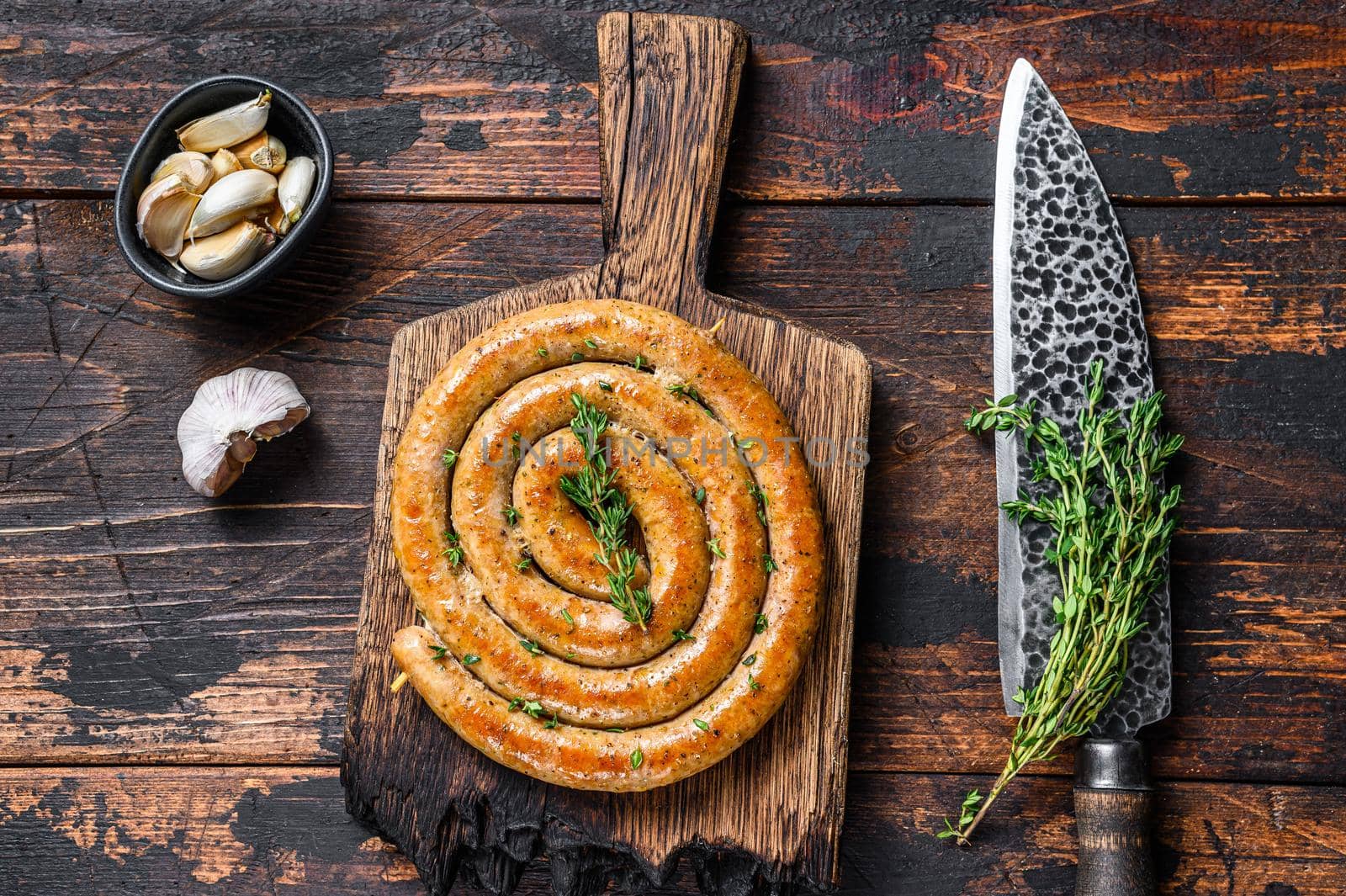 BBQ spiral sausage from pork and beef meat on a wooden cutting board. Dark wooden background. Top view by Composter