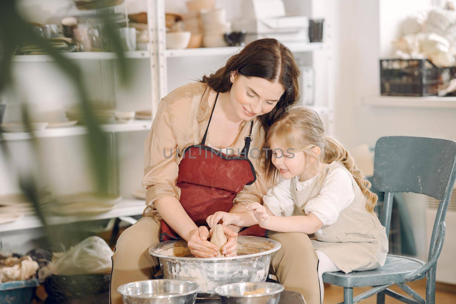 Woman and girl kneading clay. Family make art product at table in pottery workshop. Mother with daughter.