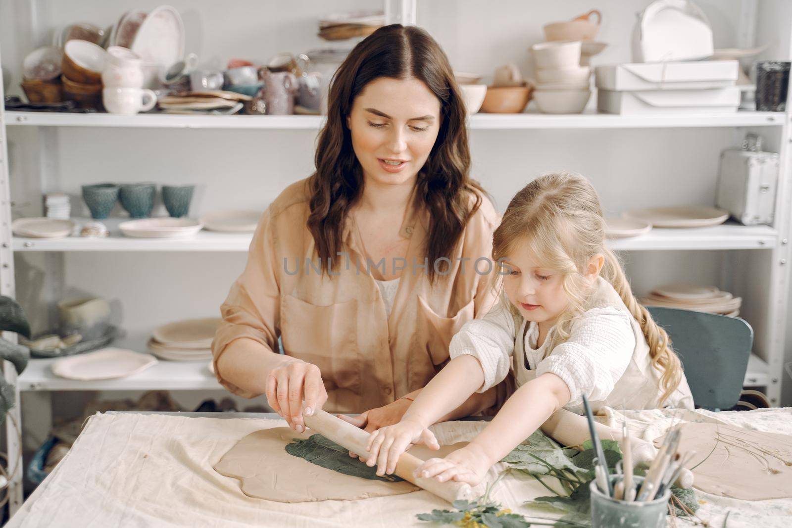 Woman and girl kneading clay. Family make art product at table in pottery workshop. Mother with daughter.