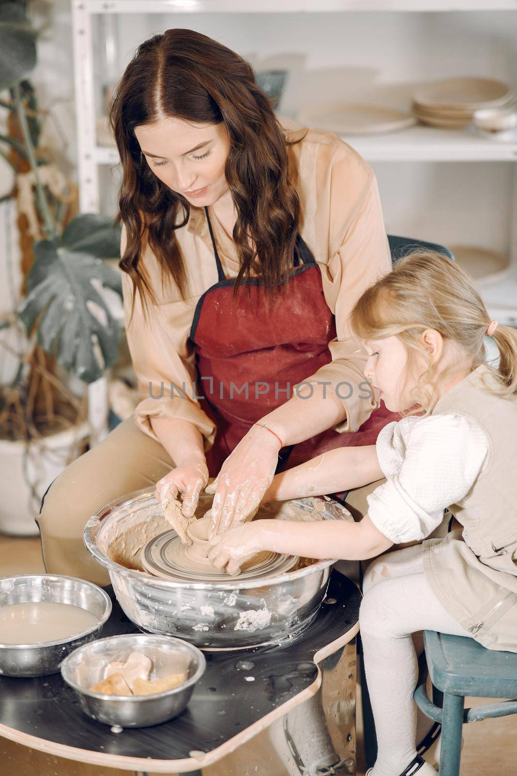 Woman and girl kneading clay. Family make art product at table in pottery workshop. Mother with daughter.