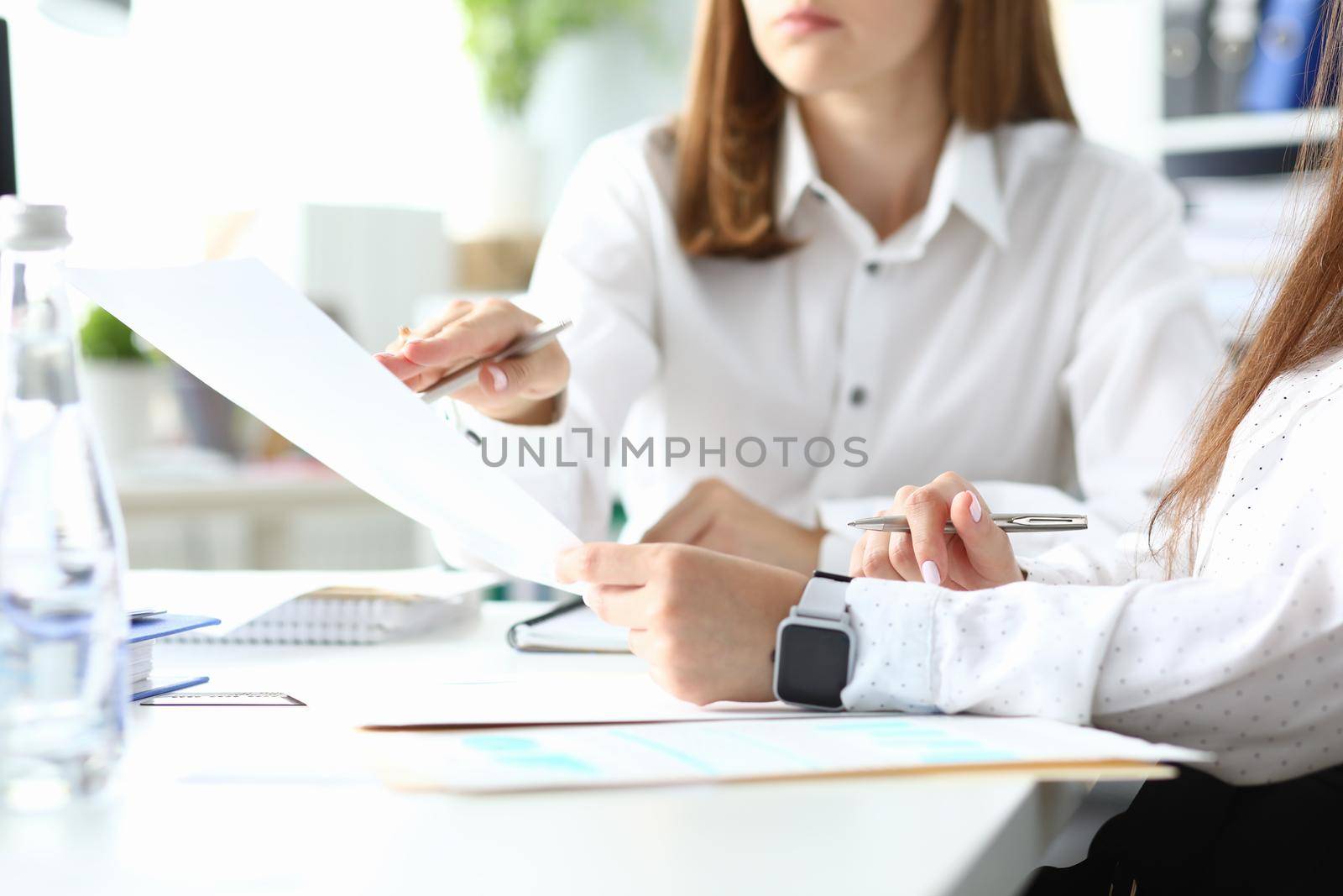 Focus on woman holding metallic writing pen and sitting with friendly colleague discussing something important. Businesswoman arm in watches. Accounting workplace concept. Blurred background