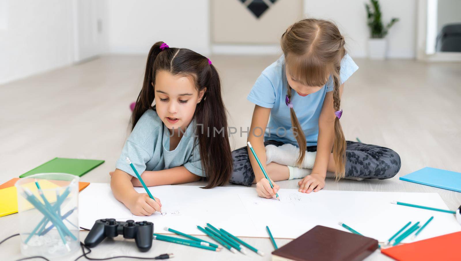 two little girls sisters lie on the floor of the house and draw with colored pencils on paper. children do creative homework after school.