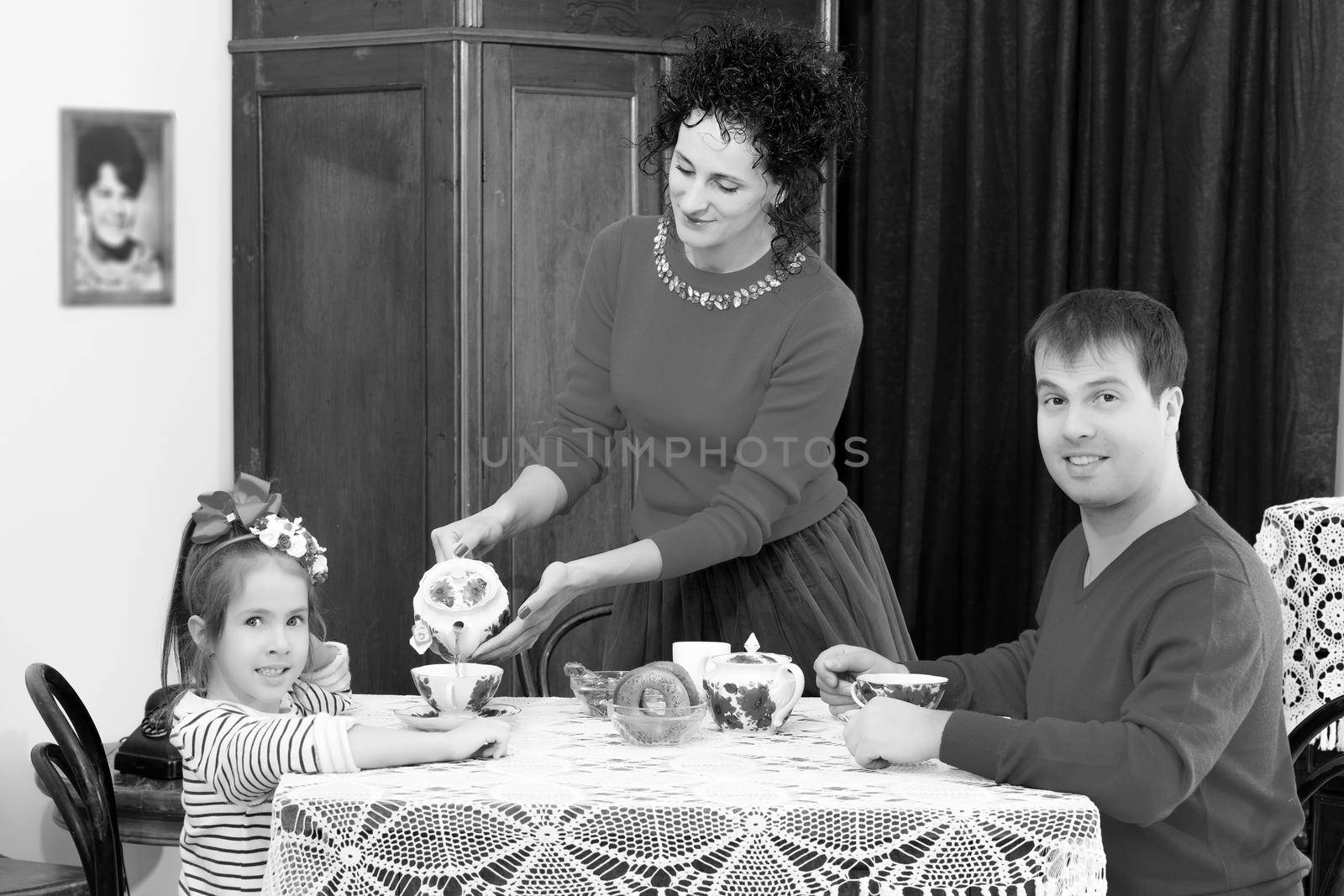 A family of three in the interior of the fifties of the last century, drinking tea for lace tablecloth vintage oak table.Black-and-white photo. Retro style.